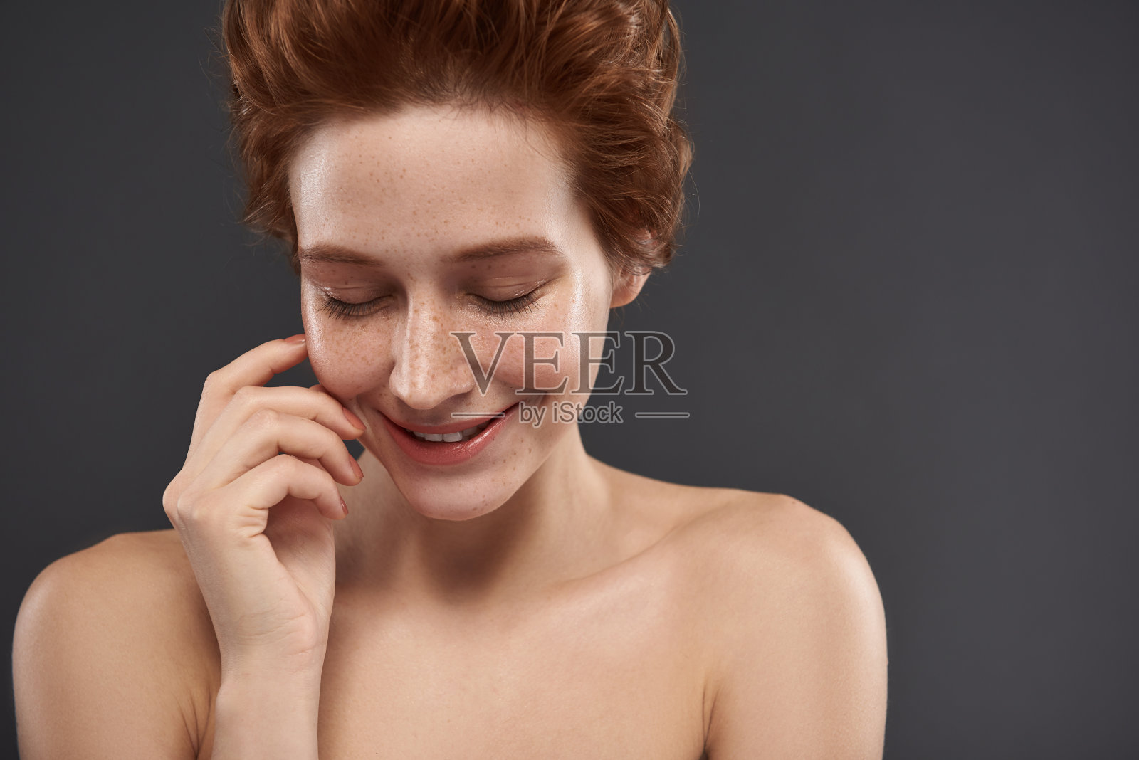 可爱的红头发女孩闭着眼睛站在灰色的背景照片摄影图片