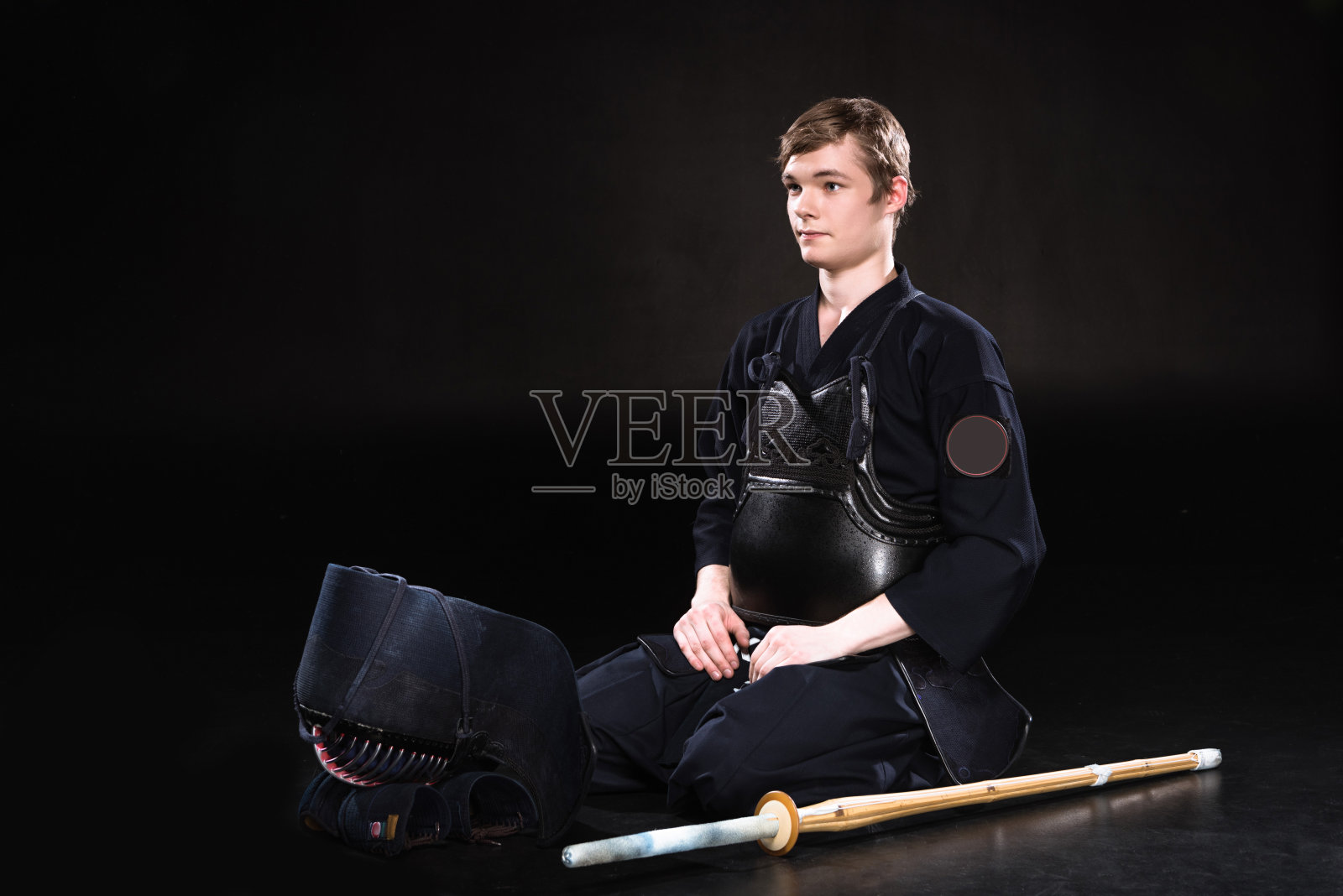 一名身穿剑道铠甲，头戴钢盔，手持竹剑的青年，坐在黑衣上照片摄影图片