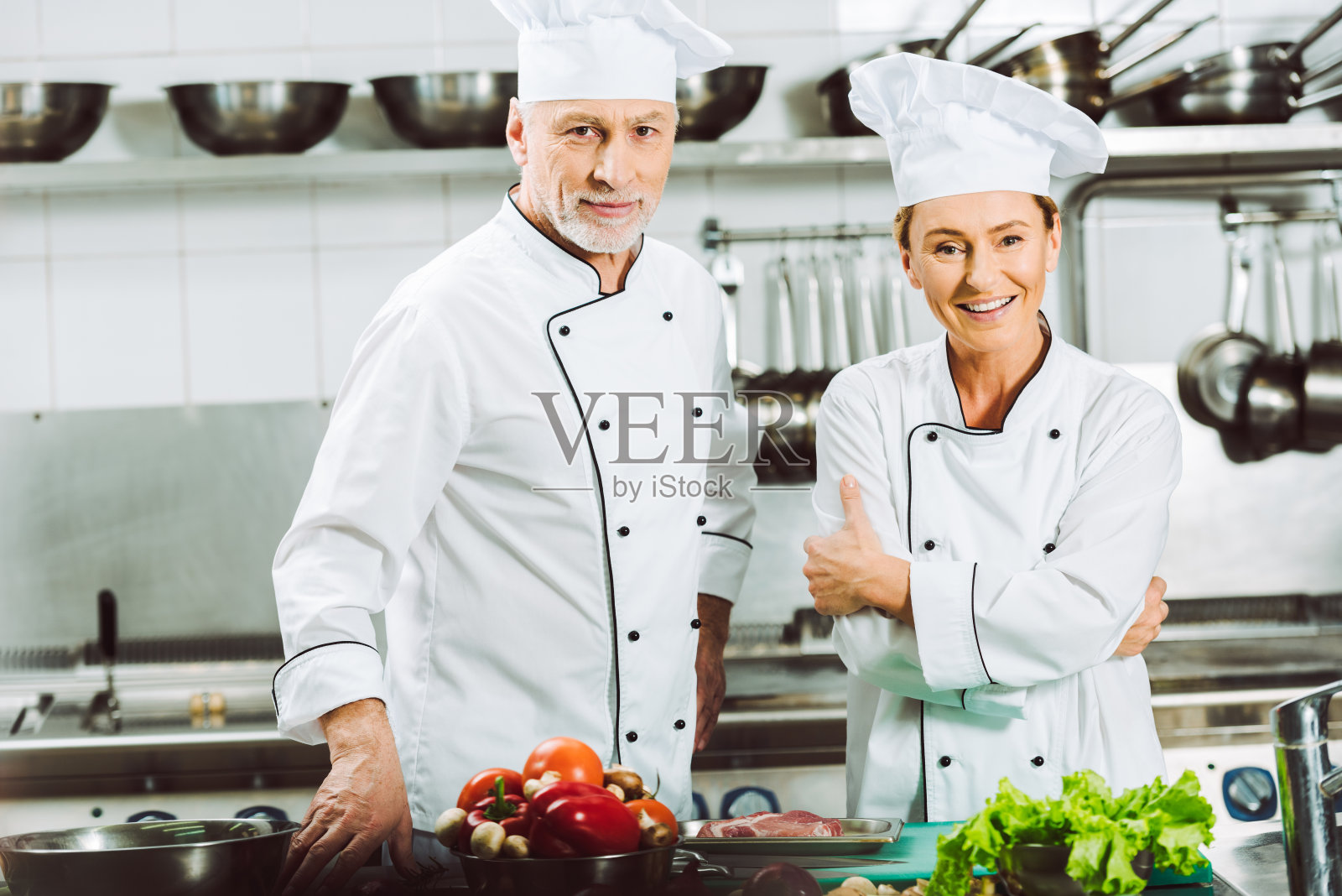 微笑的女厨师和男厨师穿着制服和帽子看着摄像机在餐厅厨房做饭照片摄影图片