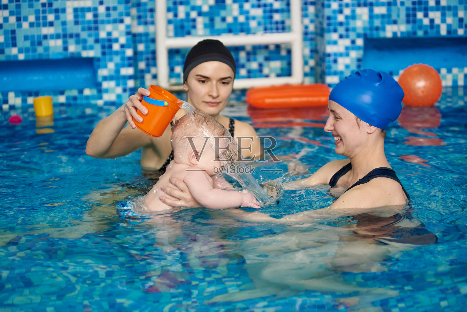 健康的家庭母亲教婴儿游泳，教练帮助在游泳池。教练为妈妈和宝宝进行课程照片摄影图片