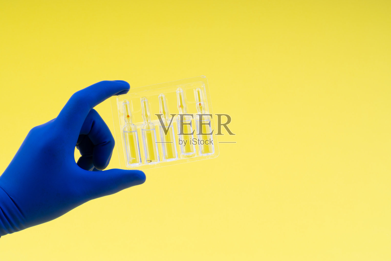 以黄色为底色，手持装有医用安瓿瓶的蓝色手套照片摄影图片