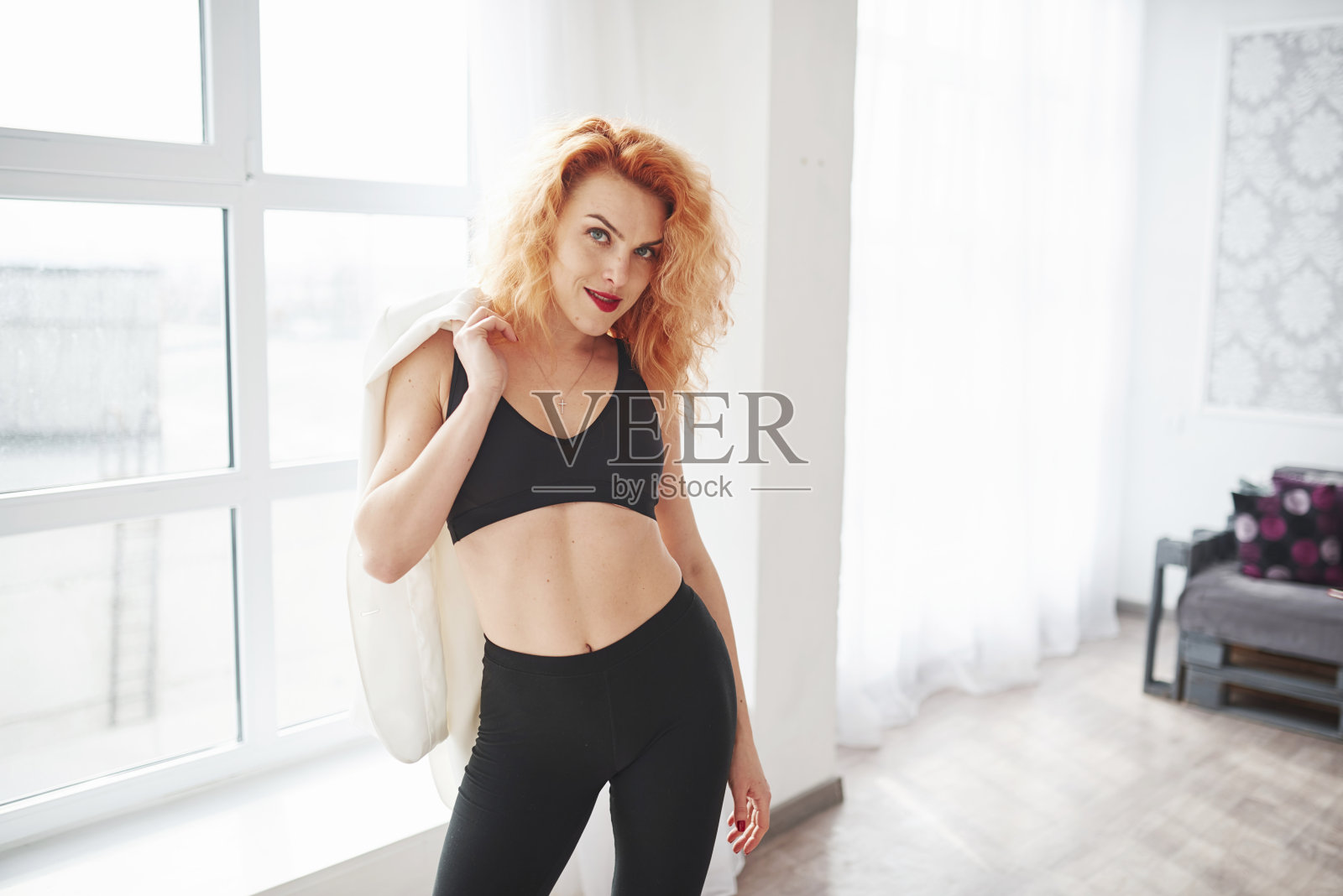 温暖的温度。有魅力的红发女人在靠近窗户的空间里摆姿势照片摄影图片