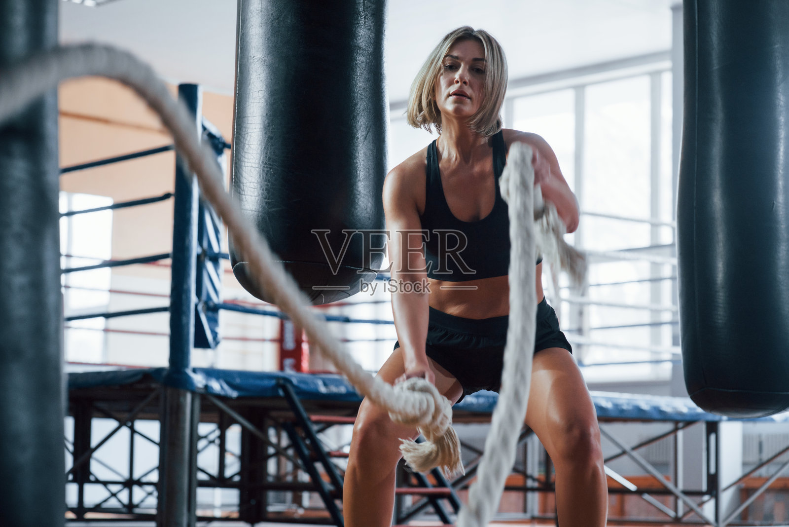 努力工作。金发女运动员在体育馆里用绳子锻炼。强壮的女性照片摄影图片
