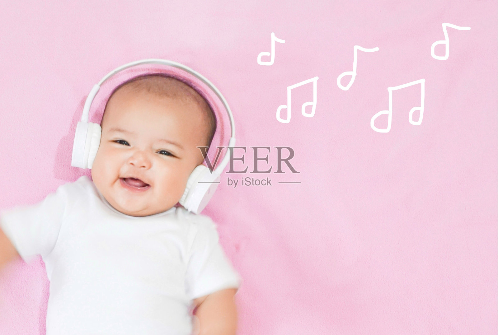 亚洲女婴戴着白色耳机，白色衬衫，粉红色背景照片摄影图片