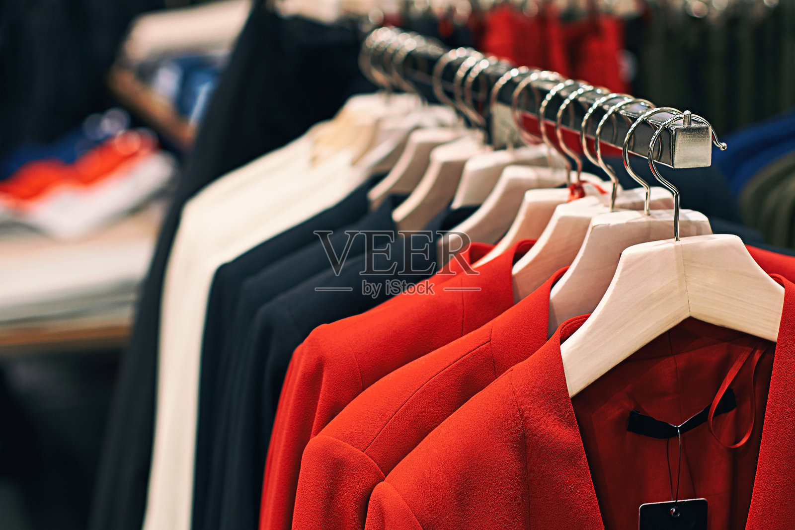 在服装零售店里，女夹克挂在衣架上，有红、蓝、白等颜色。照片摄影图片