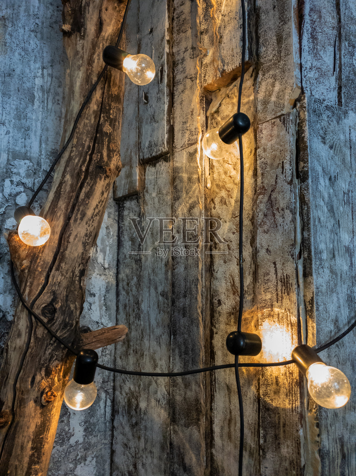 房间里有一面浅色的木板墙，树干上挂着一个灯泡花环。黄色暖灯泡。照片摄影图片