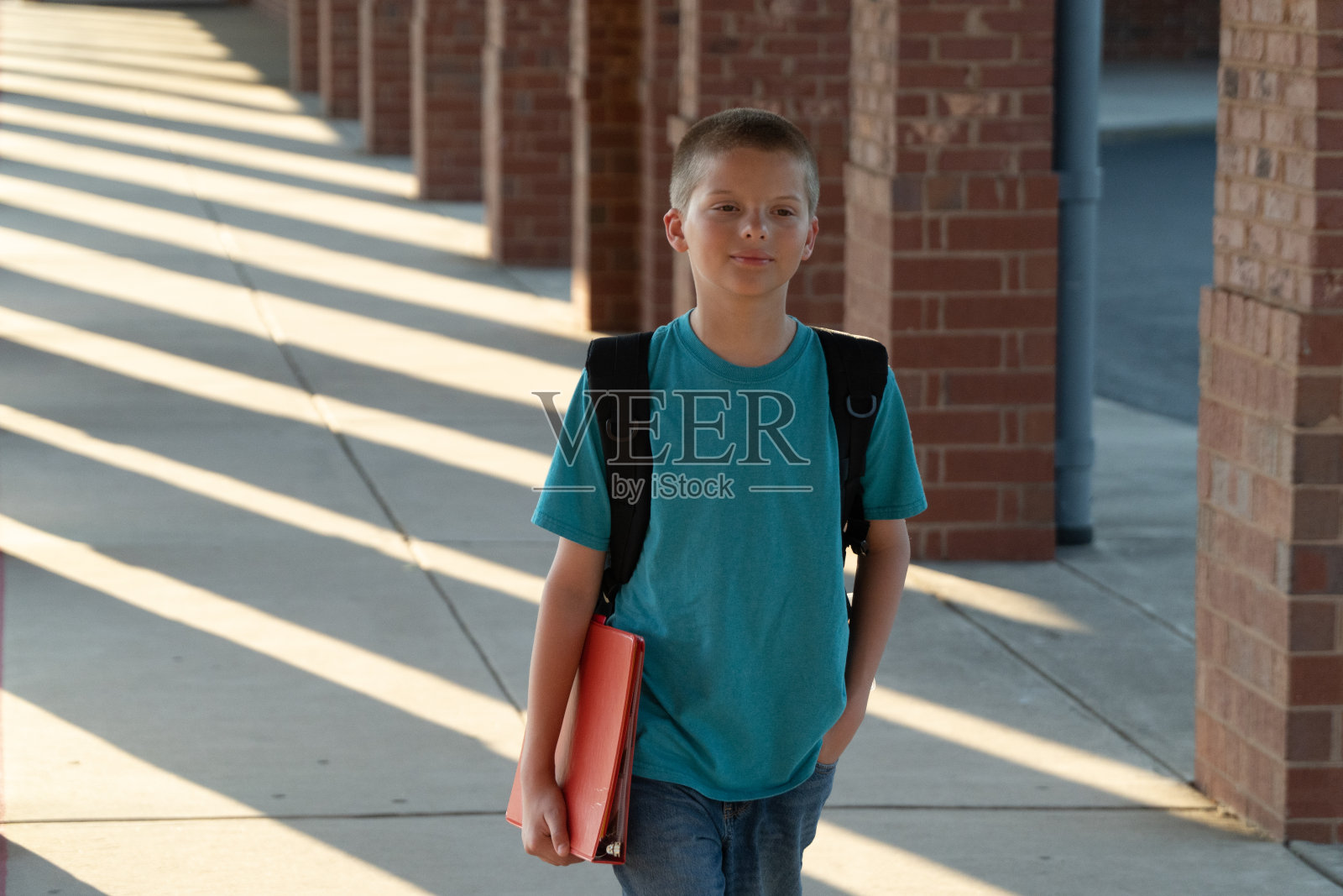 小男孩带着活页夹和背包回到学校。照片摄影图片