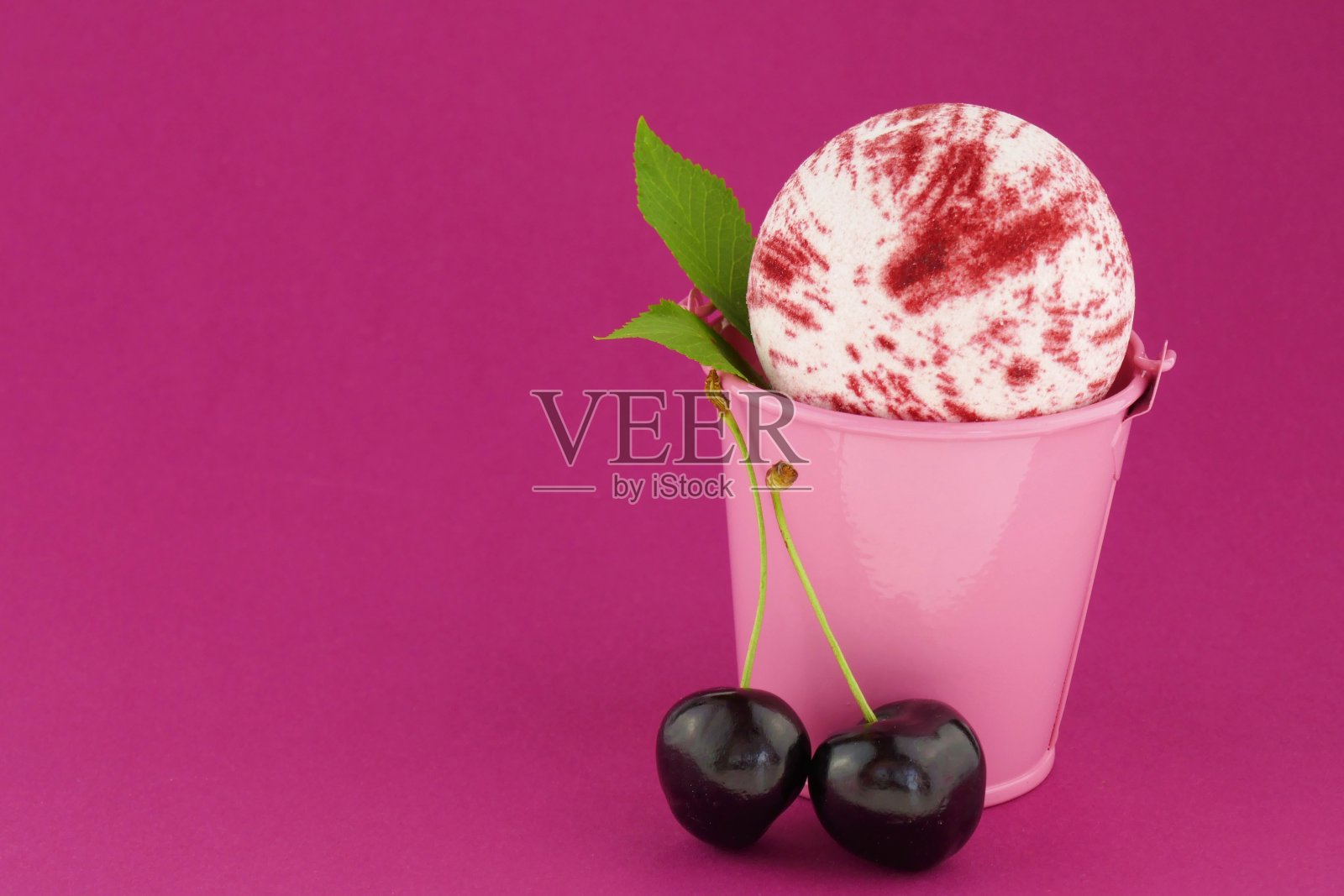 甜樱桃提取物沐浴炸弹。条纹炸弹沐浴在一个粉红色装饰桶，成熟的樱桃浆果在明亮的粉红色背景。有机浆果身体化妆品照片摄影图片