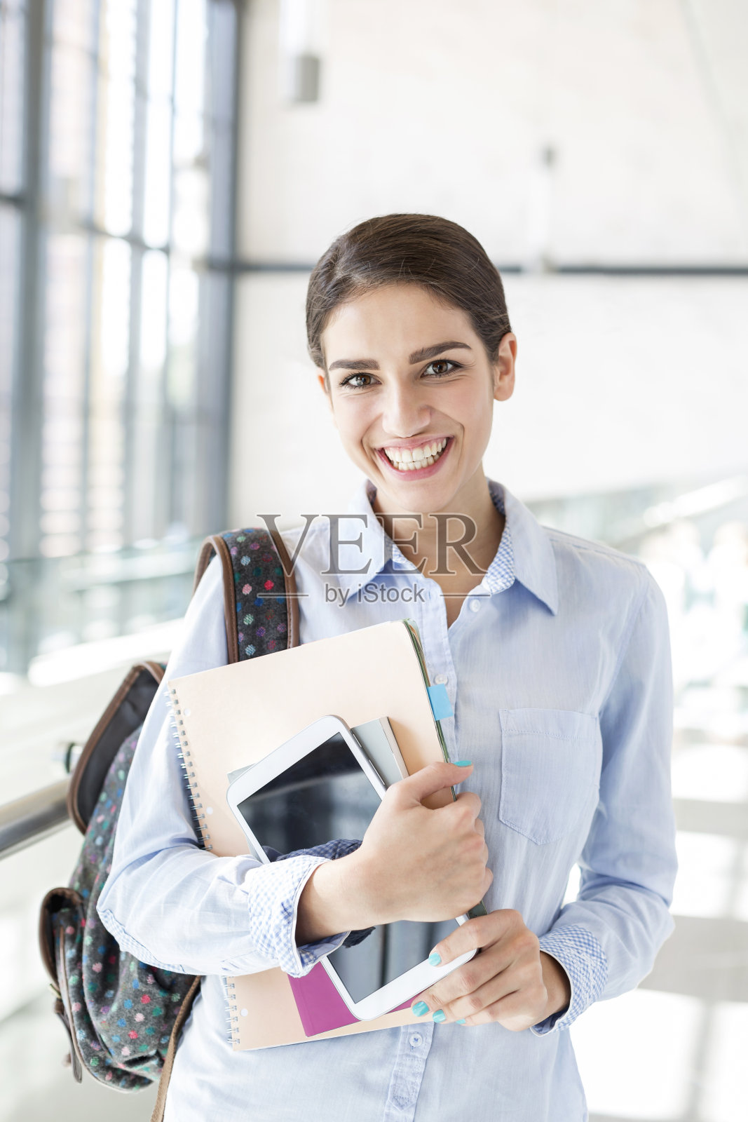少女在大学走廊手持书籍与平板电脑照片摄影图片