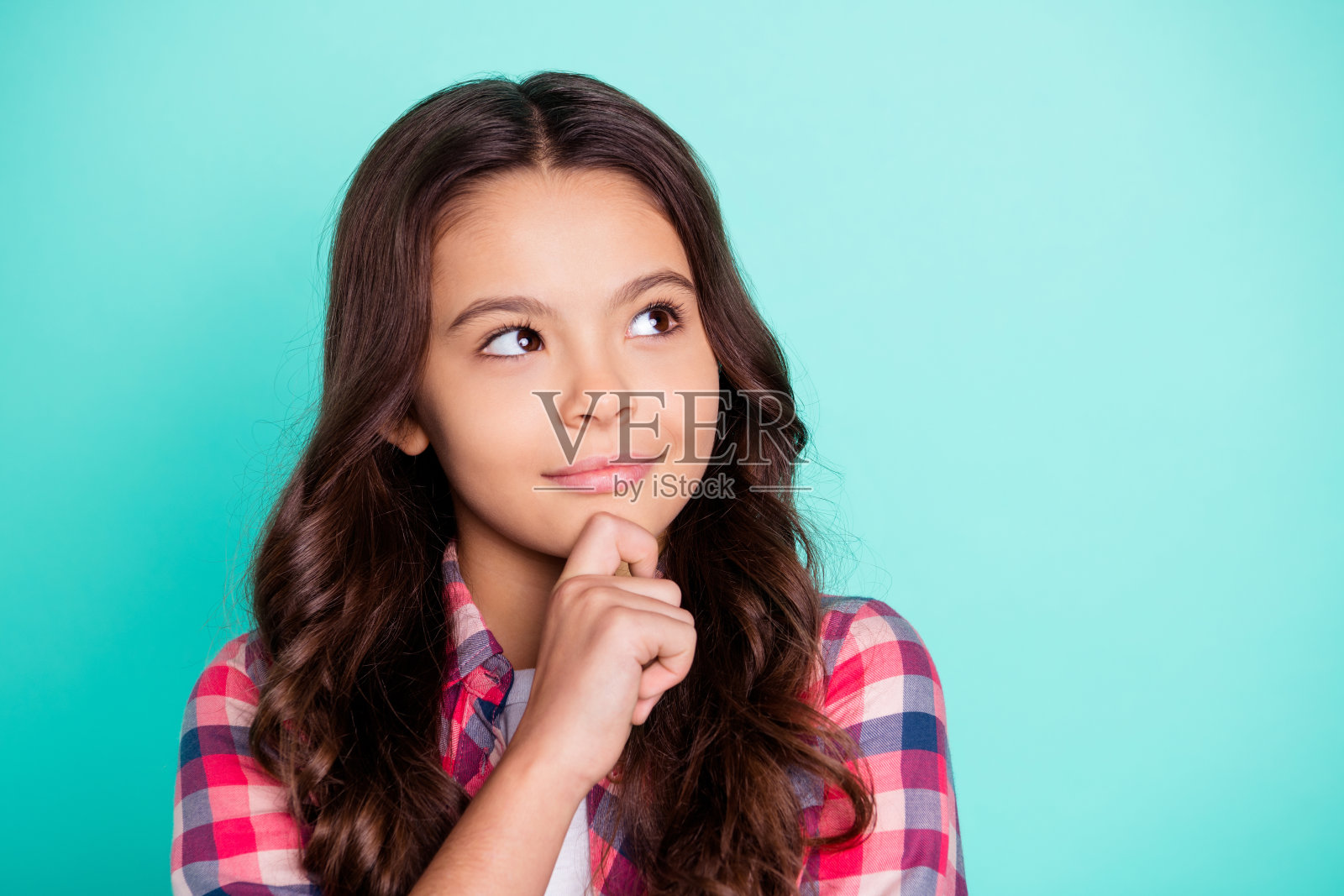她的特写肖像，她漂亮，迷人，可爱，甜美，聪明，卷曲的头发，十几岁的女孩穿着格子衬衫，思考触摸下巴孤立在明亮生动的亮蓝色背景照片摄影图片