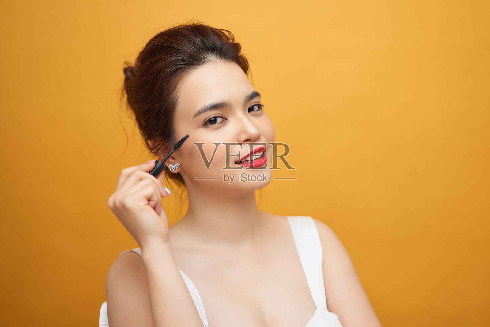 近距离的肖像迷人的年轻女子把一些睫毛膏在她的睫毛与化妆刷在黄色的背景照片摄影图片