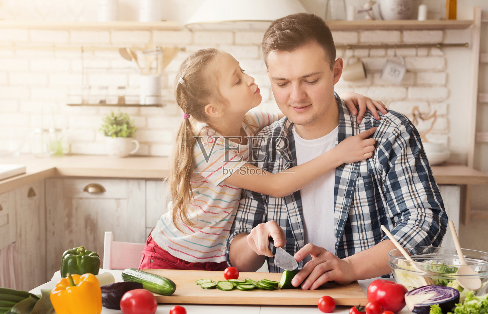 漂亮的小女孩在厨房里亲吻她父亲的脸颊照片摄影图片
