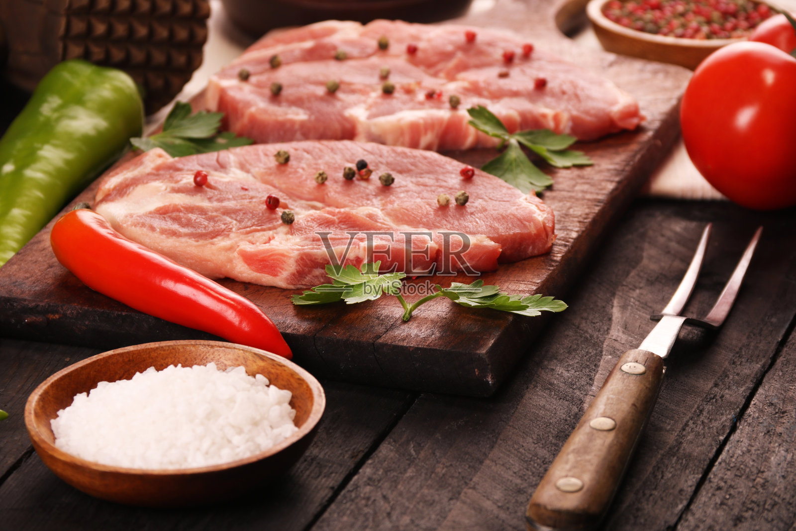 生肉。将生猪肉排放在砧板上，以黑色为背景，配以蔬菜、辣椒、番茄、盐和香料照片摄影图片