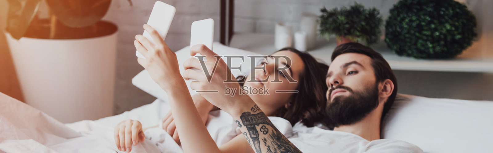 一对漂亮的年轻夫妇躺在床上玩智能手机照片摄影图片