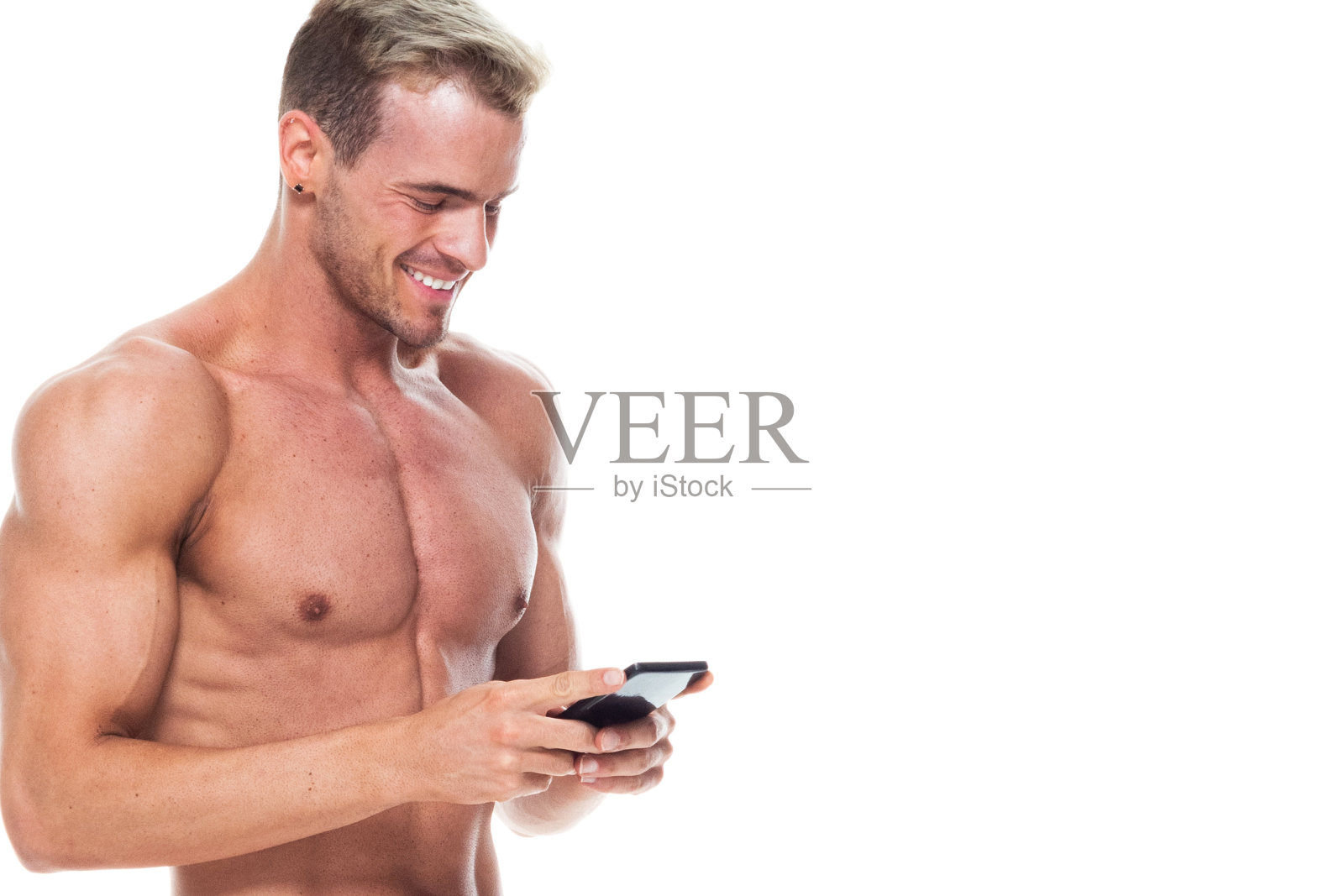 帅气的男人赤裸上身，穿着短裤，在智能手机上发短信照片摄影图片