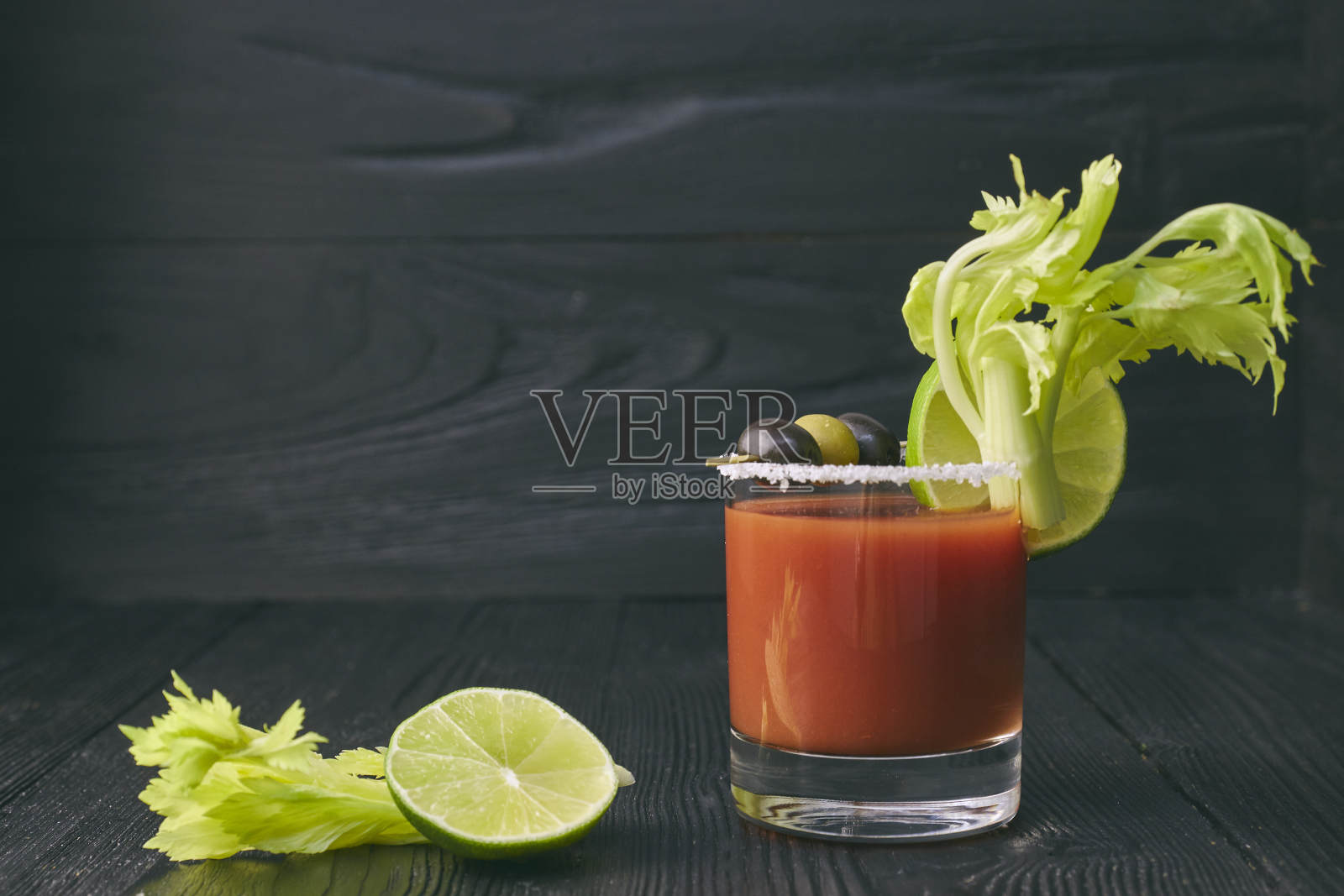 血腥鸡尾酒血腥玛丽、酸橙、芹菜、盐和零食装在一个玻璃杯里，放在黑色的木桌上。水平鸡尾酒视图照片摄影图片