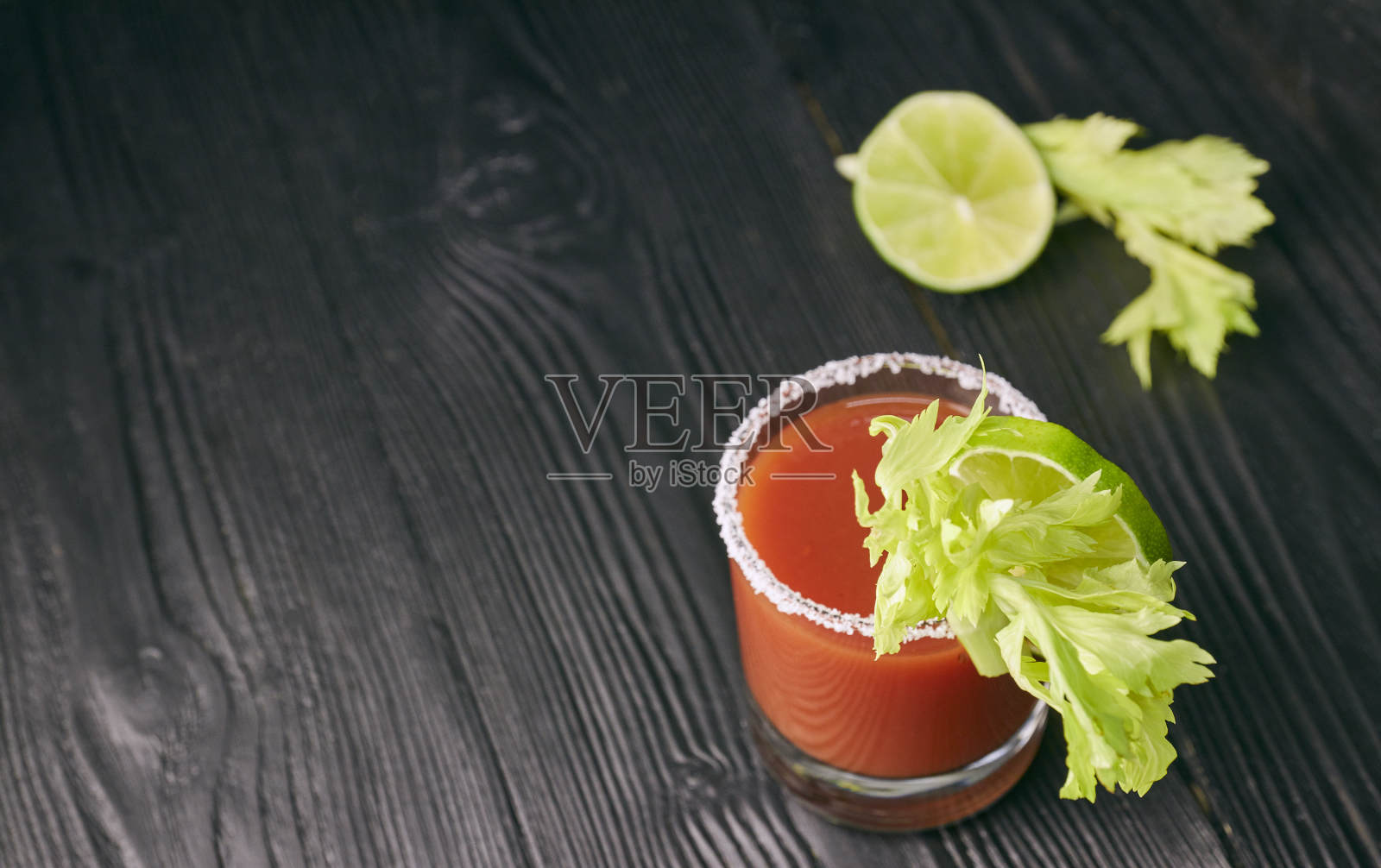 血腥鸡尾酒血腥玛丽、酸橙、芹菜、盐和零食装在一个玻璃杯里，放在黑色的木桌上。水平鸡尾酒视图照片摄影图片