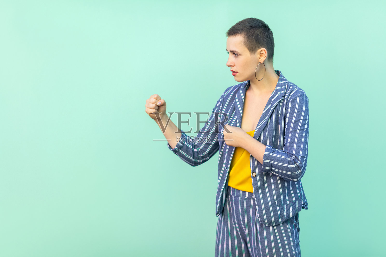 侧面的肖像严肃美丽的短发年轻时尚的女人在休闲条纹西装站与拳击拳头和看相机照片摄影图片