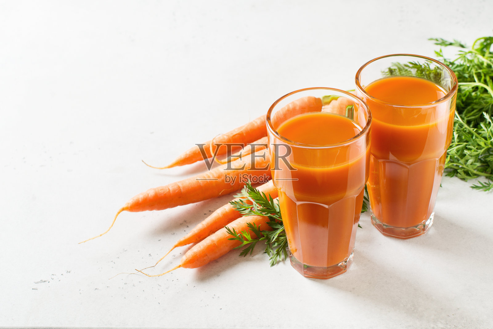 胡萝卜汁在白色的石头背景与生的和新鲜的胡萝卜照片摄影图片