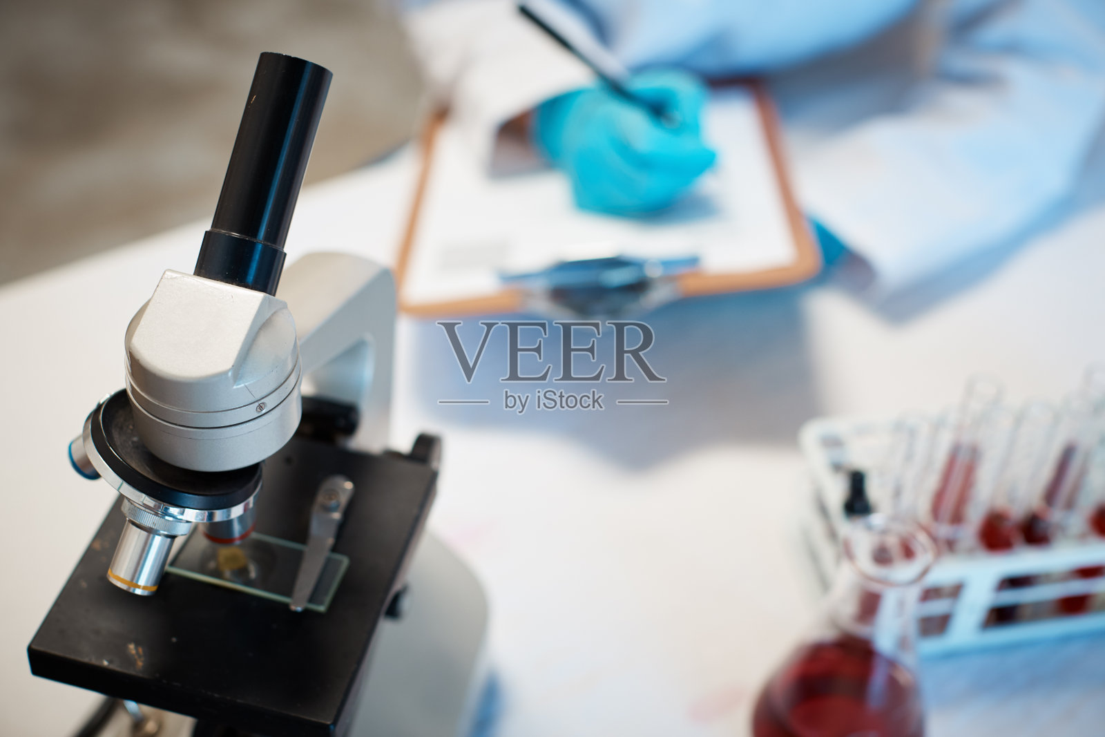 科学实验室的工作人员用显微镜在剪贴板上做笔记照片摄影图片