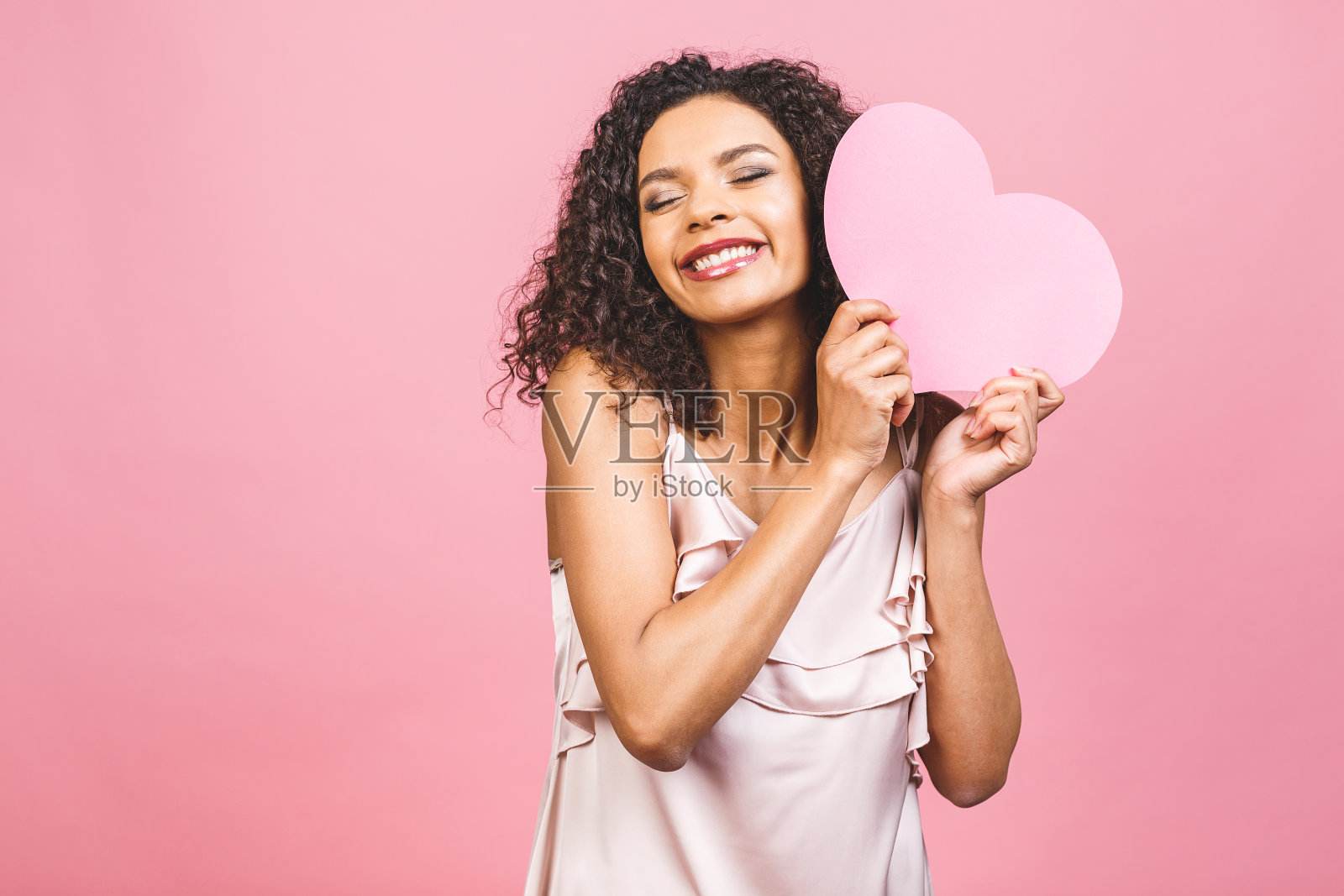 肖像迷人的快乐微笑的美国黑人妇女孤立的粉红色背景与大粉红色的心。照片摄影图片