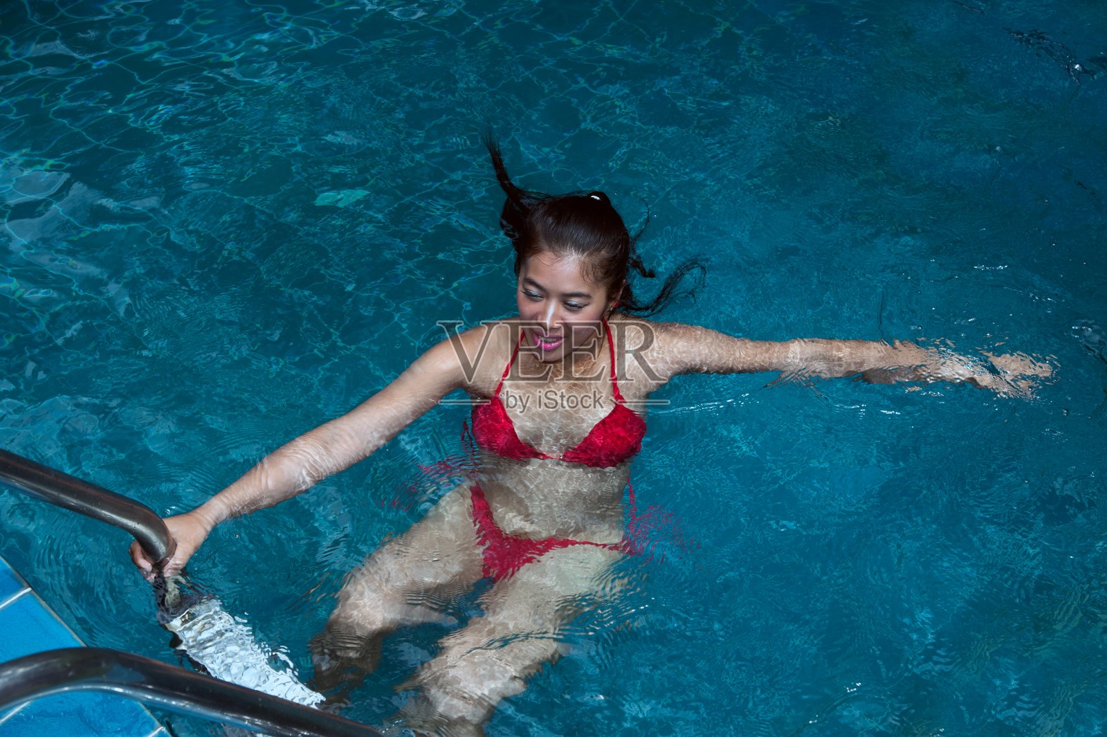 漂亮的亚洲女人穿着红色比基尼在游泳池游泳。照片摄影图片