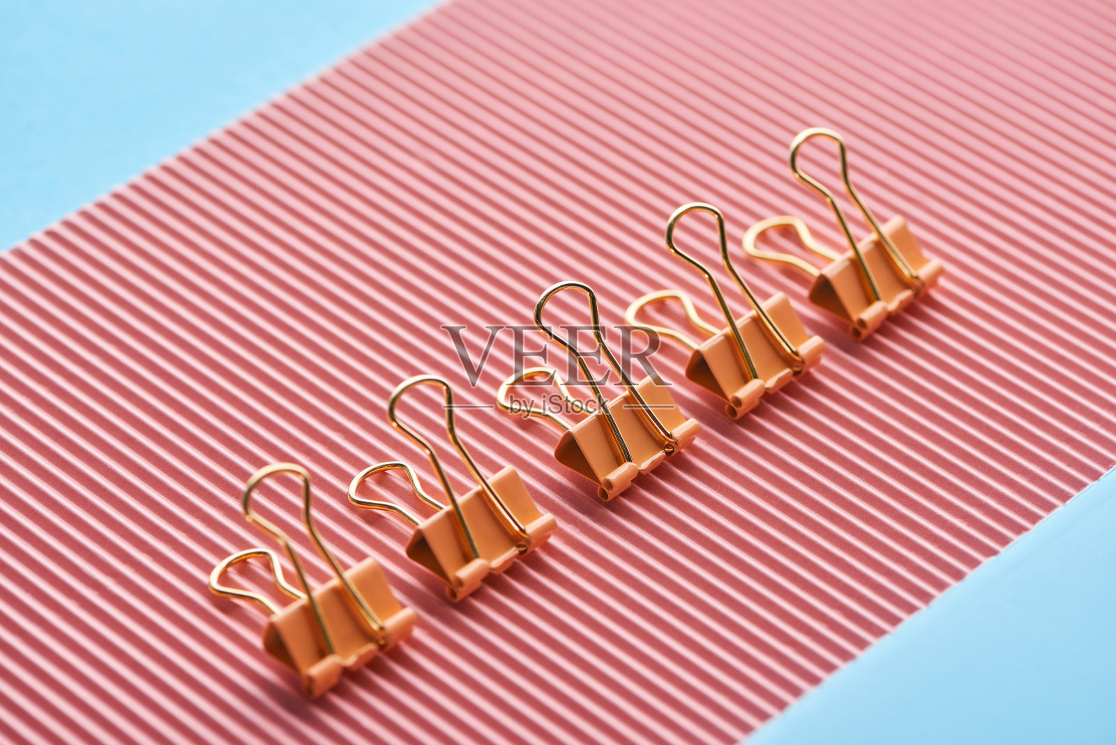 金属回形针放在有纹理的粉红色纸上，孤立在蓝色纸上照片摄影图片