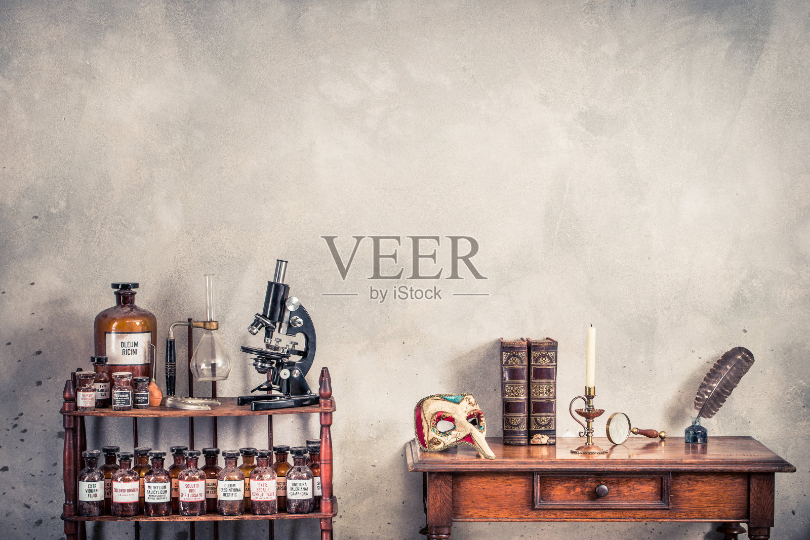 古董显微镜，木制架子上的旧实验室瓶子，嘉年华面具，羽毛笔，墨水瓶，书籍，放大镜，橡木桌子上的古董烛台上的蜡烛。复古风格滤镜照片照片摄影图片