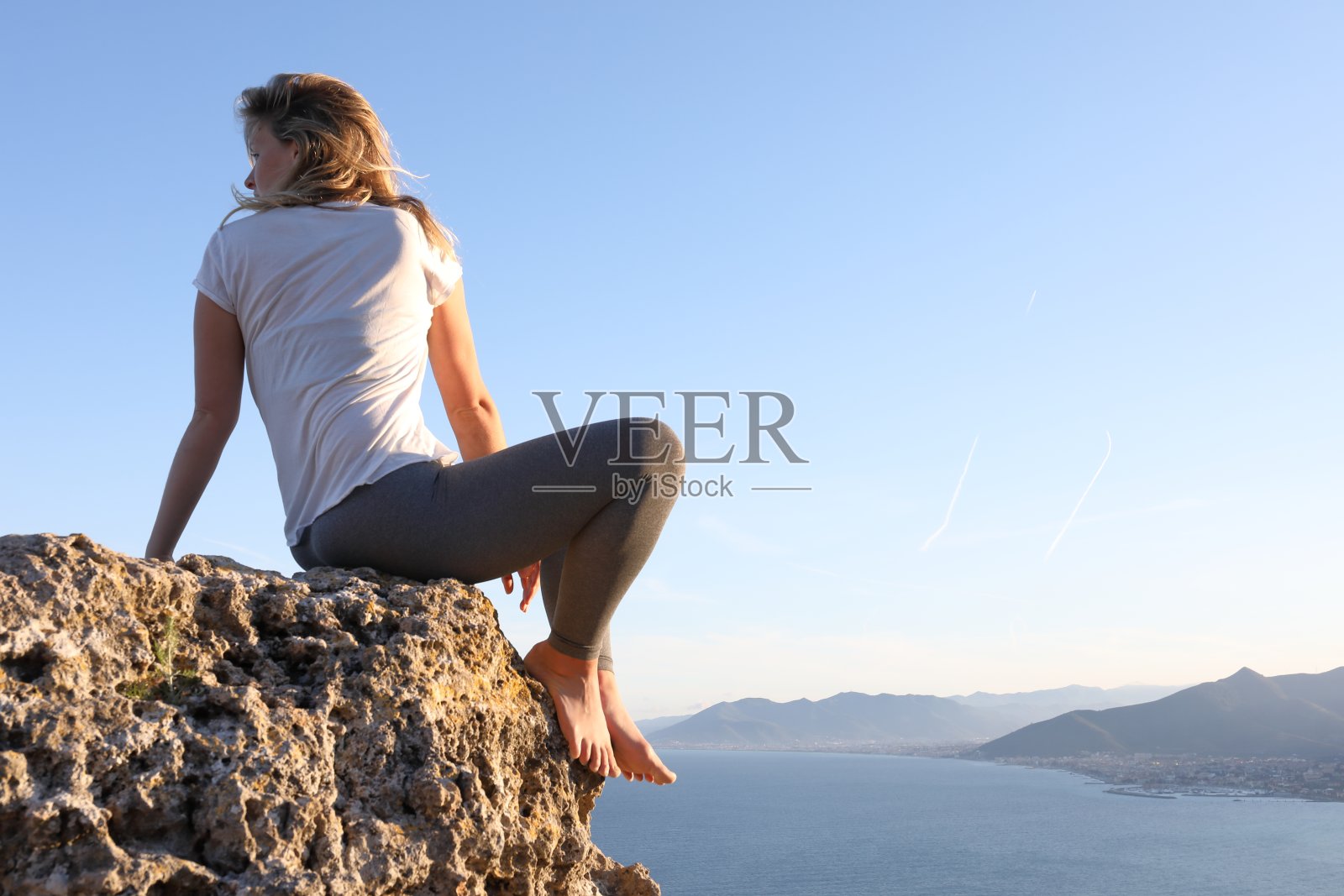 日出时分，年轻女子在海岸线上的悬崖上休息照片摄影图片
