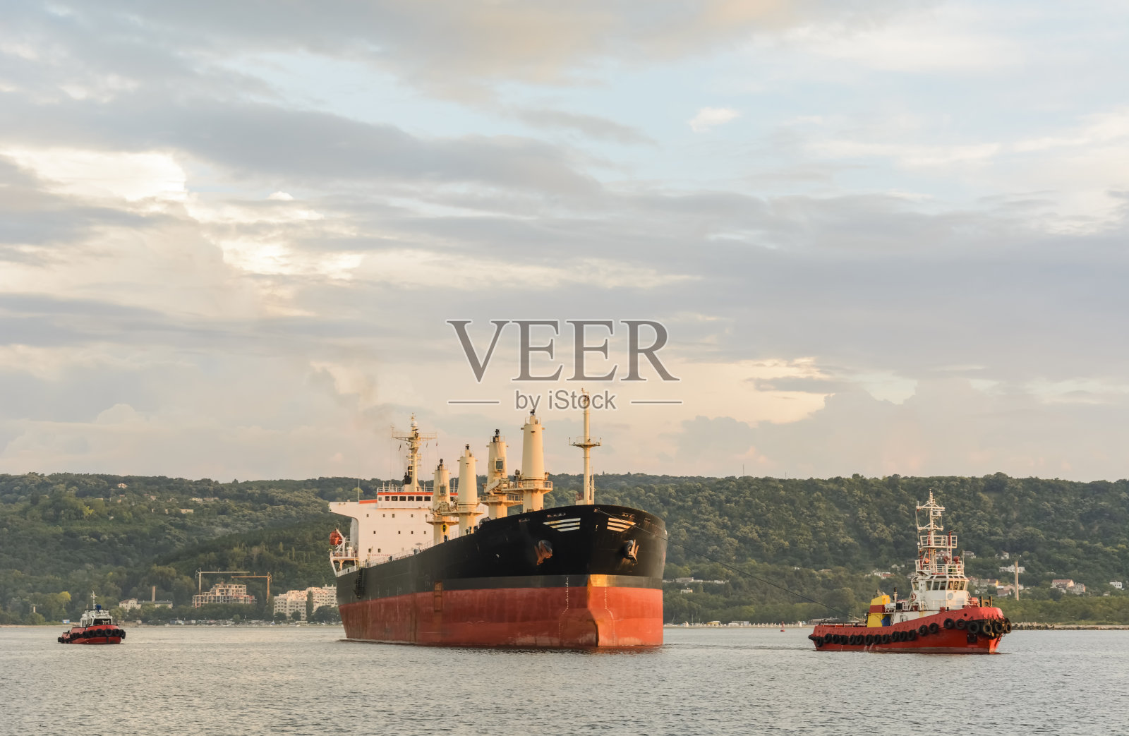 拖船载着大型货轮进港。照片摄影图片