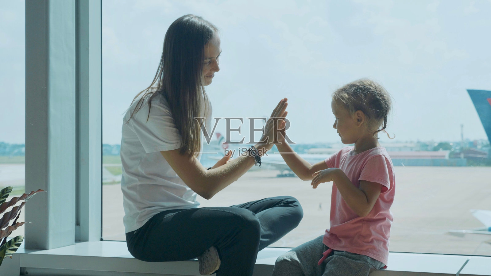 年轻的妈妈和可爱的女儿在机场玩得很开心。照片摄影图片