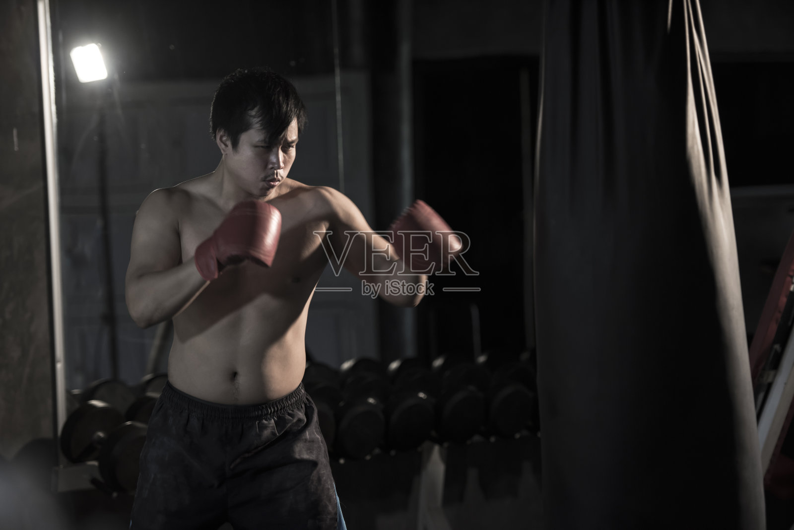 一个年轻的亚洲人在健身房用沙袋练习拳击的肖像。照片摄影图片