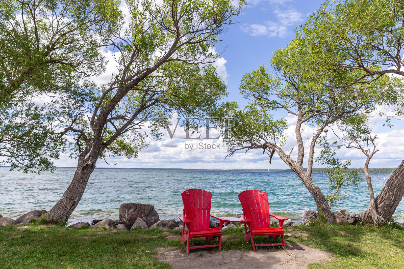 湖边有两把红色的木制草坪椅。照片摄影图片