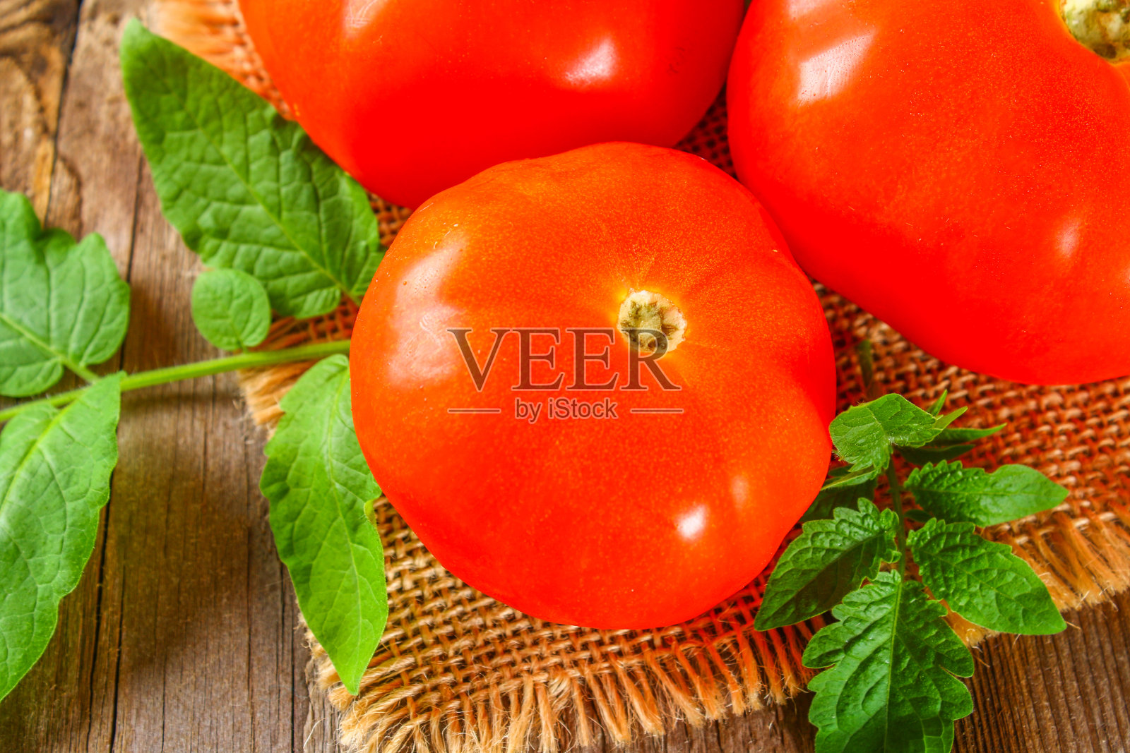 旧木桌上放着新鲜的西红柿和叶子。照片摄影图片