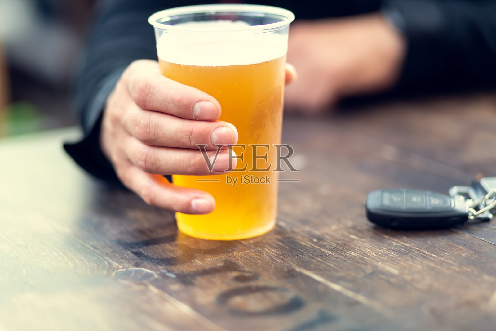 男人喝着啤酒，车钥匙在桌子上。酒后驾车的概念。照片摄影图片