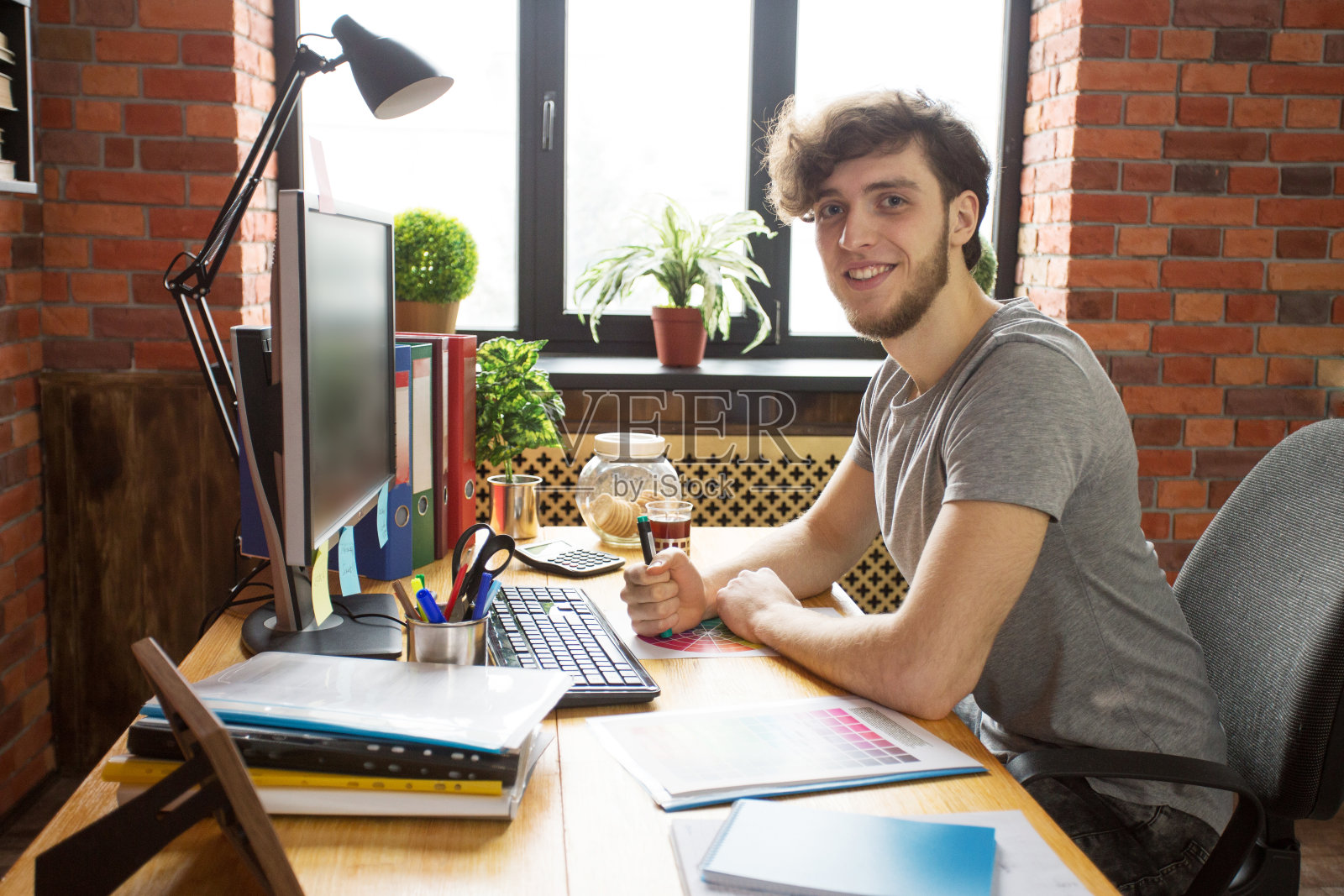 微笑的年轻男子在他的工作场所，坐在窗前，拿着标记照片摄影图片