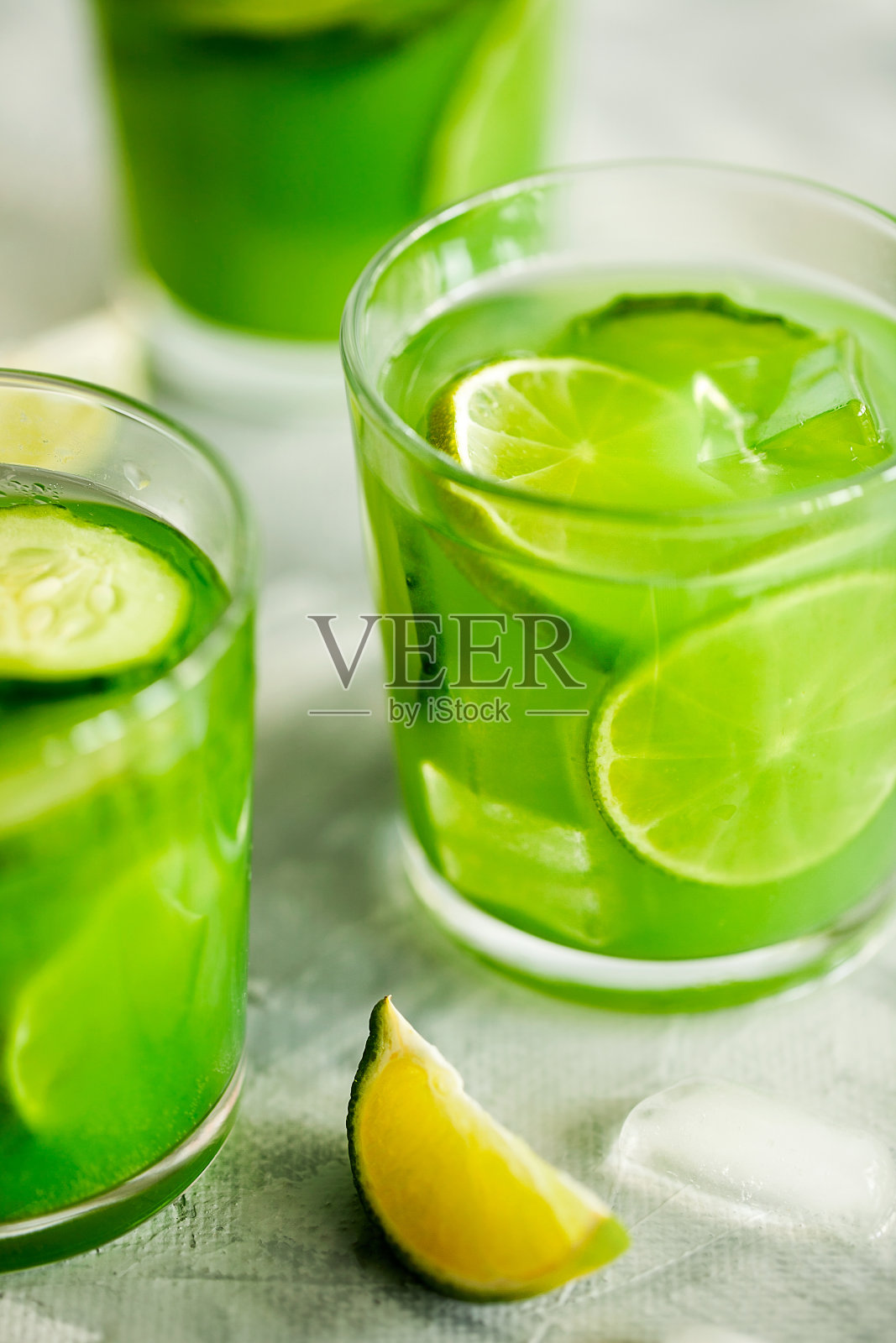 自制的时髦冰抹茶、绿茶或柠檬汁配黄瓜和酸橙在浅灰色的背景特写。炎热夏日的健康冷素食饮料。超级食物饮料照片摄影图片