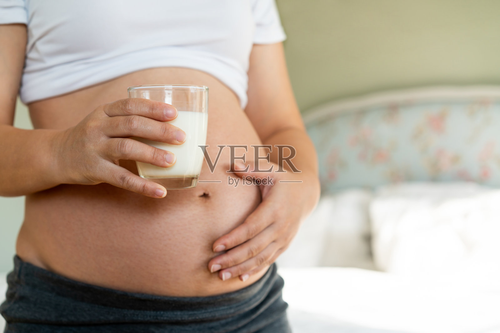快乐的孕妇在家喝牛奶，照顾孩子，年轻的准妈妈怀抱着宝宝，补充钙质照片摄影图片
