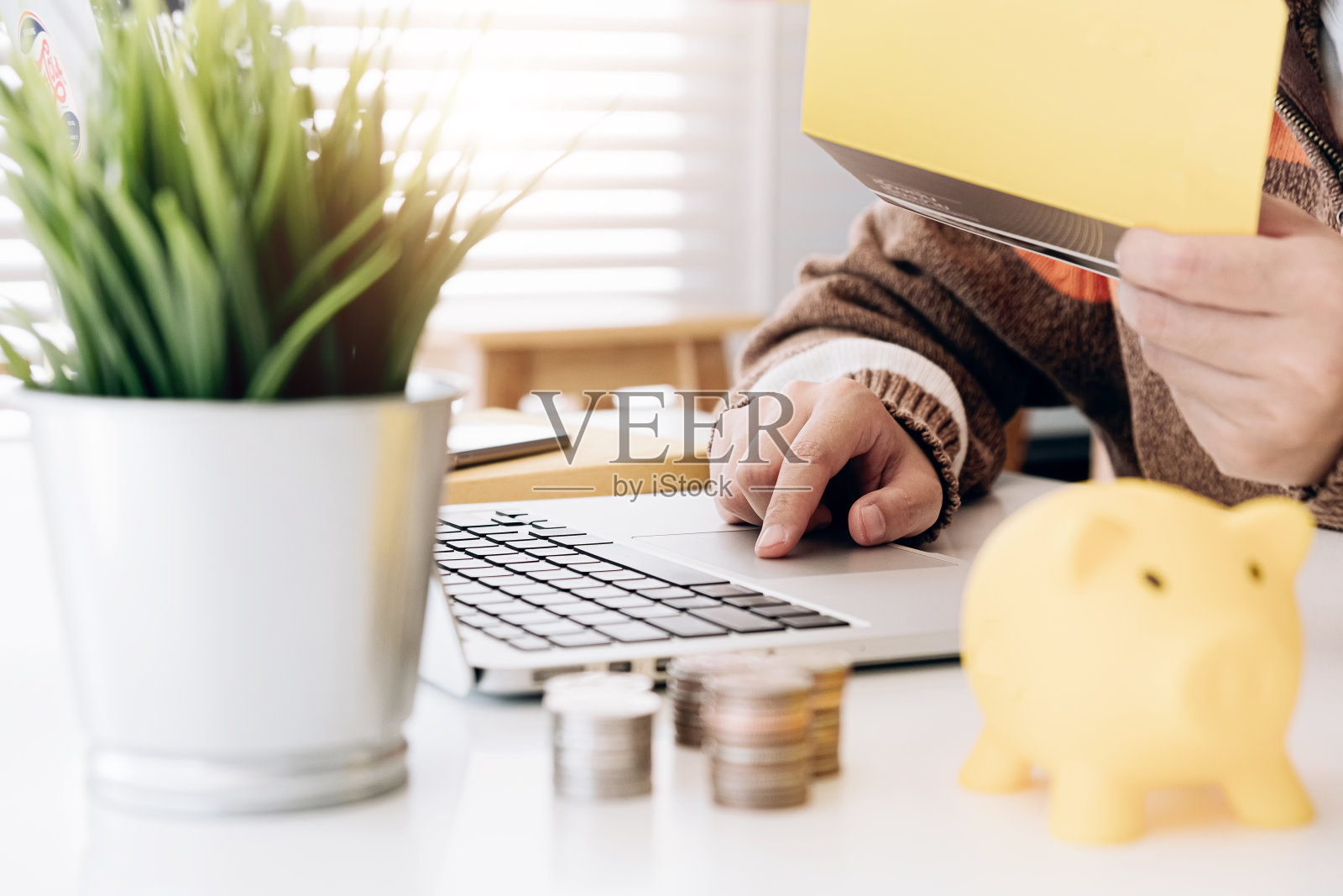 一个女人把硬币在黄色的存钱罐，同时使用笔记本电脑计算器存钱-财务储蓄概念照片摄影图片