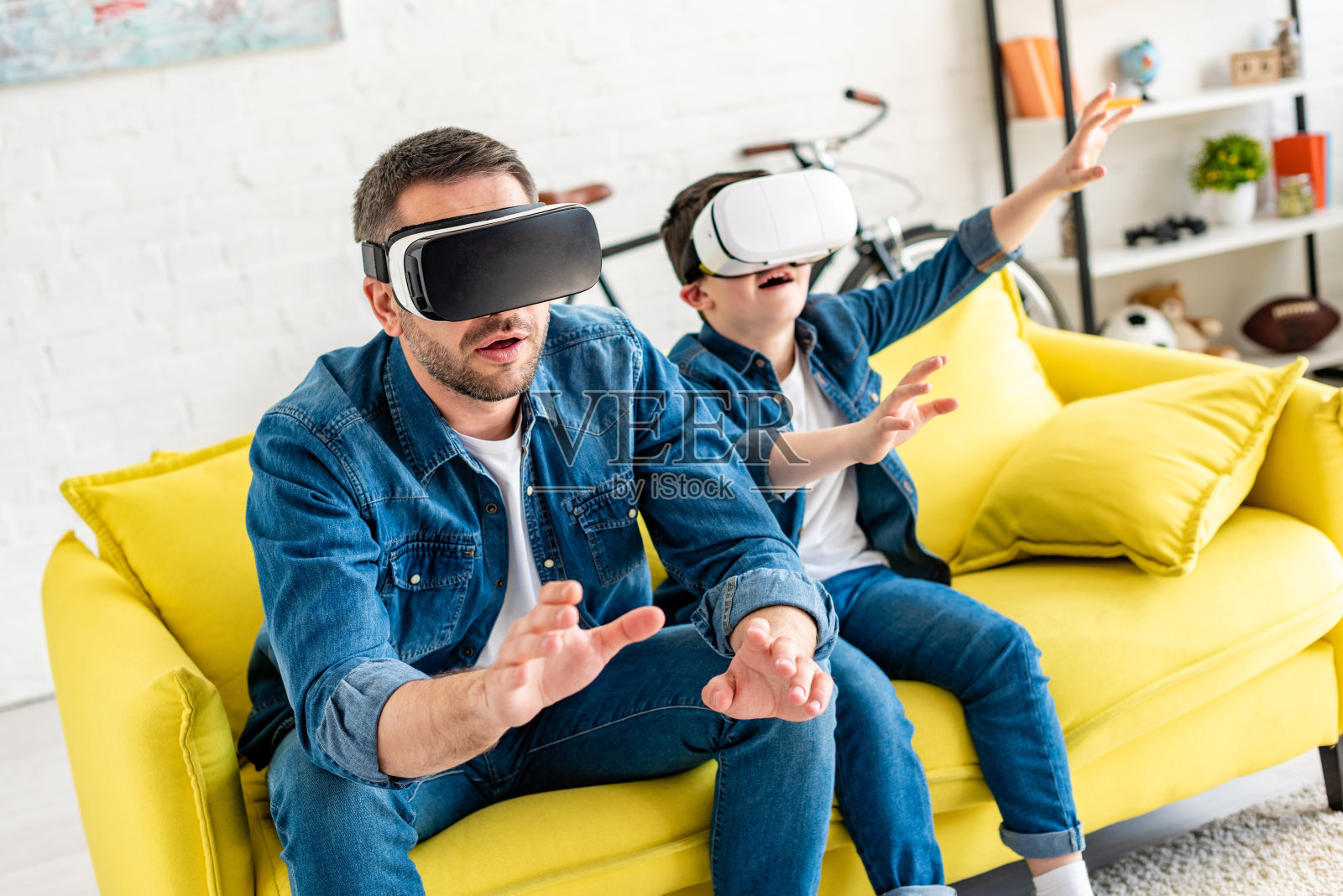 父子俩戴着虚拟头盔在家沙发上体验虚拟现实照片摄影图片