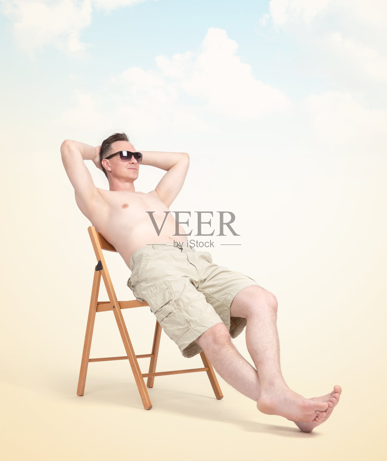 快乐的男人穿着短裤和太阳镜在沙滩上的椅子上休息，在浅黄色的背景照片摄影图片