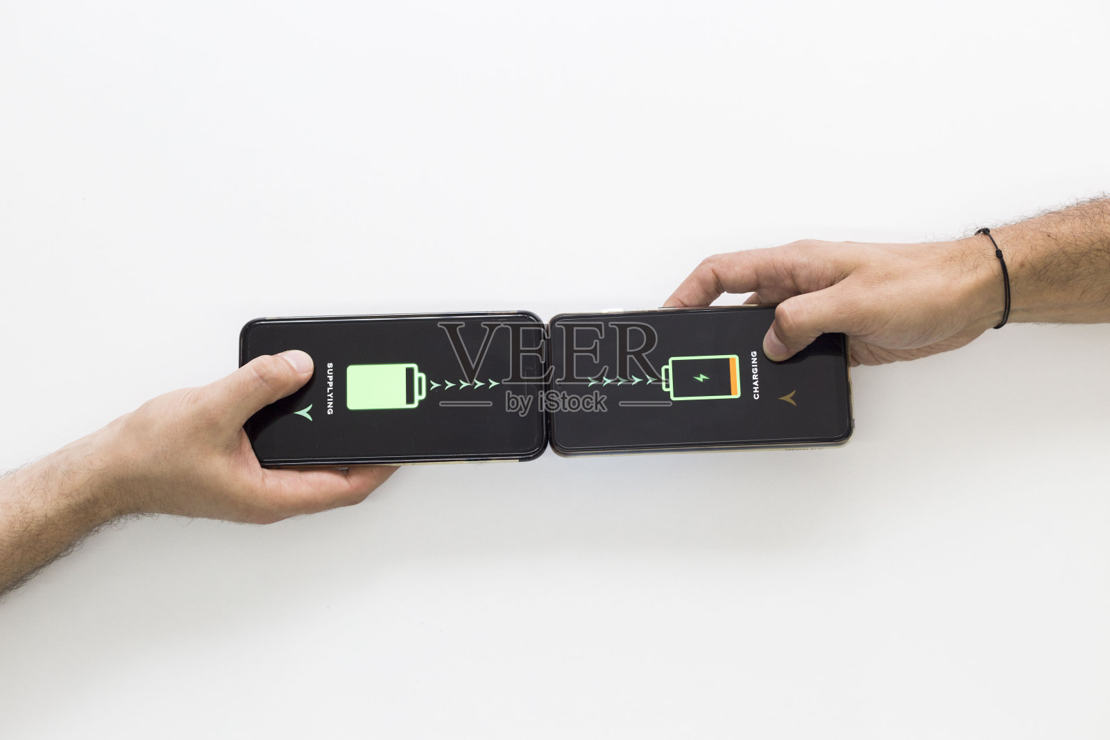 两只手拿着黑色智能手机，正在无线充电。智能手机无线充电。他们互相供应。白色背景。照片摄影图片