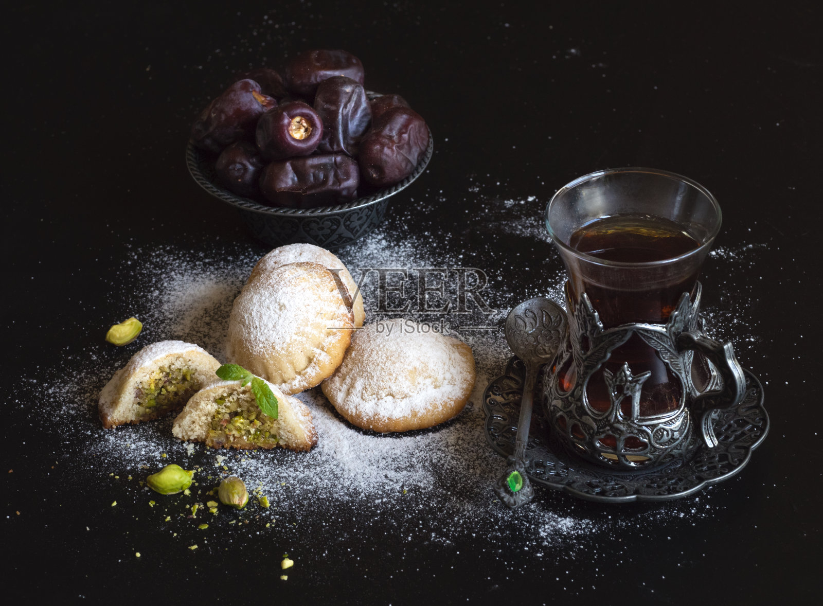 黑色的桌子上放着埃及古尔邦节饼干、椰枣和一杯茶。伊斯兰节日的饼干照片摄影图片