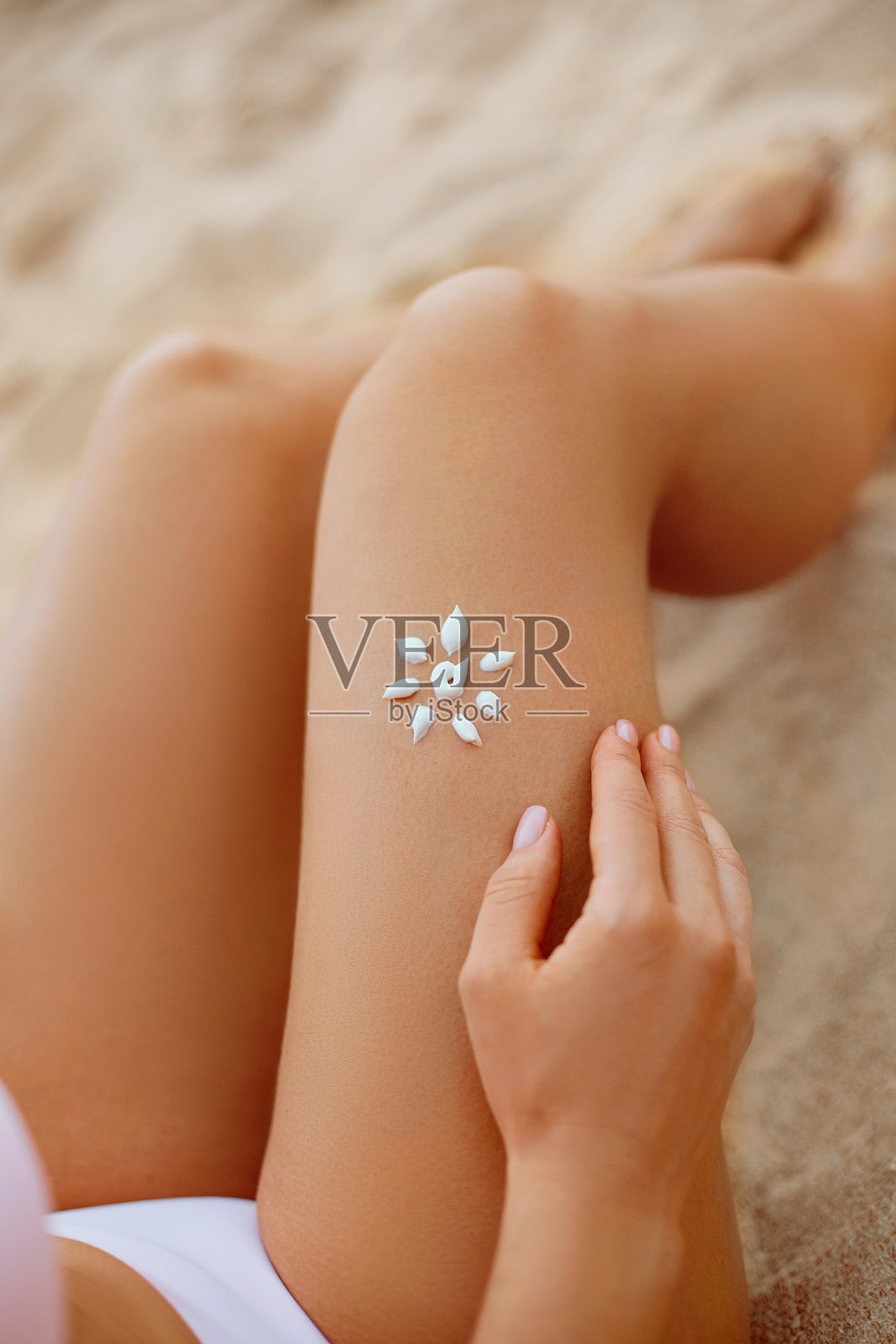 年轻女子与太阳形状在美丽的腿上拿着太阳霜瓶在海滩上。防晒霜，涂在她光滑的晒黑的腿上。防晒霜。护肤品照片摄影图片