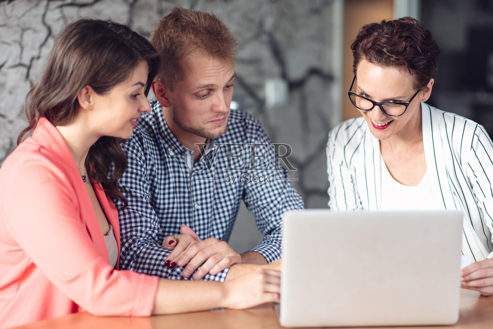 一位投资顾问正在给坐在她办公室办公桌前的一对友好微笑的年轻夫妇做演示照片摄影图片