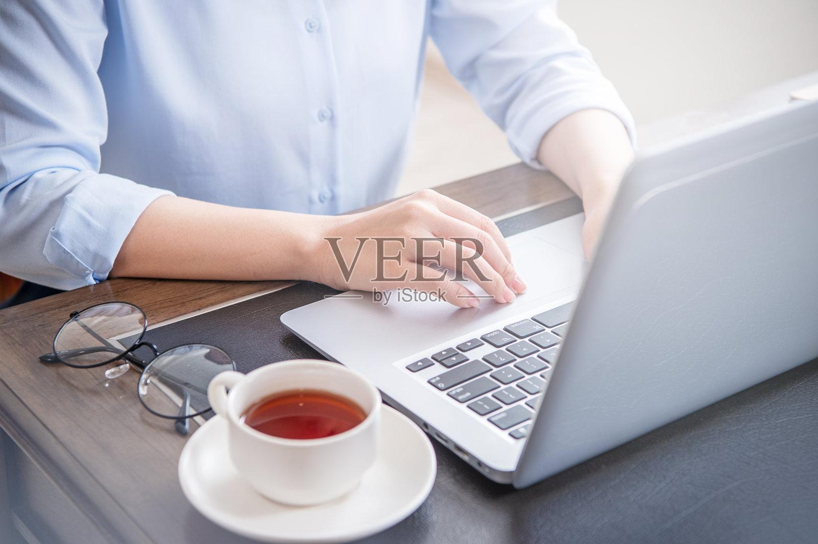 经营理念。穿着蓝色衬衫的女人在电脑上打字，咖啡放在办公桌上，背光，太阳眩光效果，近距离，侧视图，复印空间照片摄影图片
