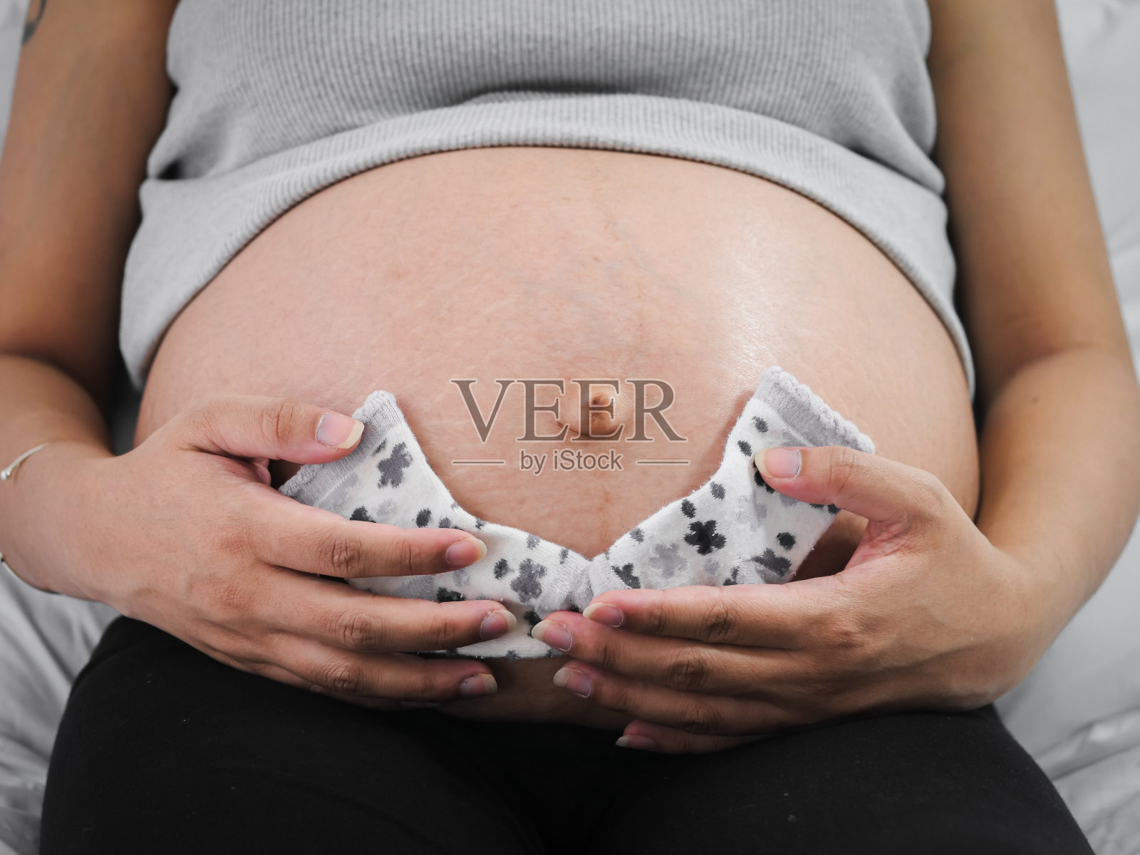 孕妇手拿粉色袜子放在肚子上，生活方式概念照片摄影图片