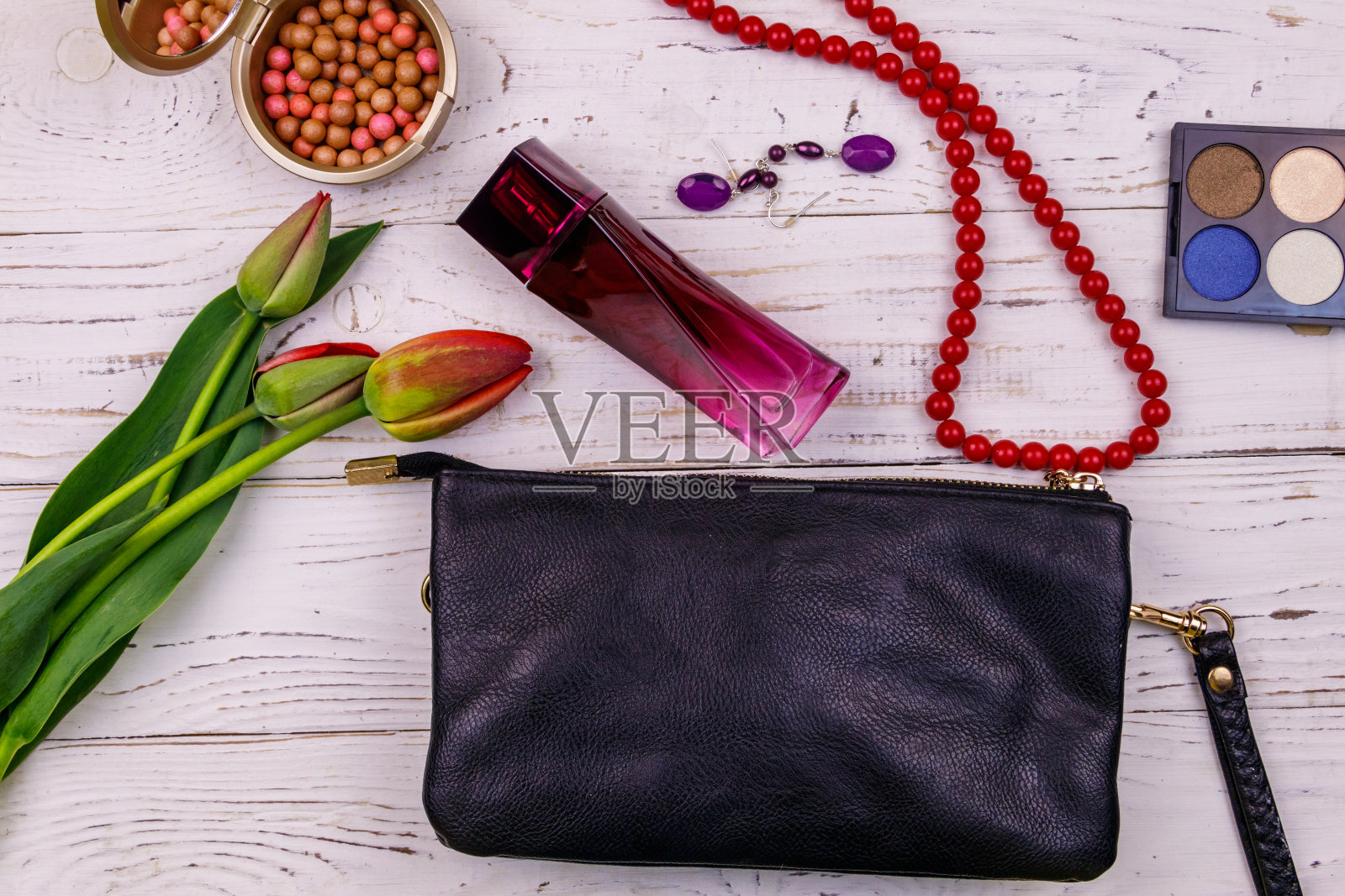 女人的配饰和化妆品在白色的木制背景上。手包、香水、眼影、胭脂球、项链、耳环和郁金香。美丽时尚的构图。俯视图，平放照片摄影图片