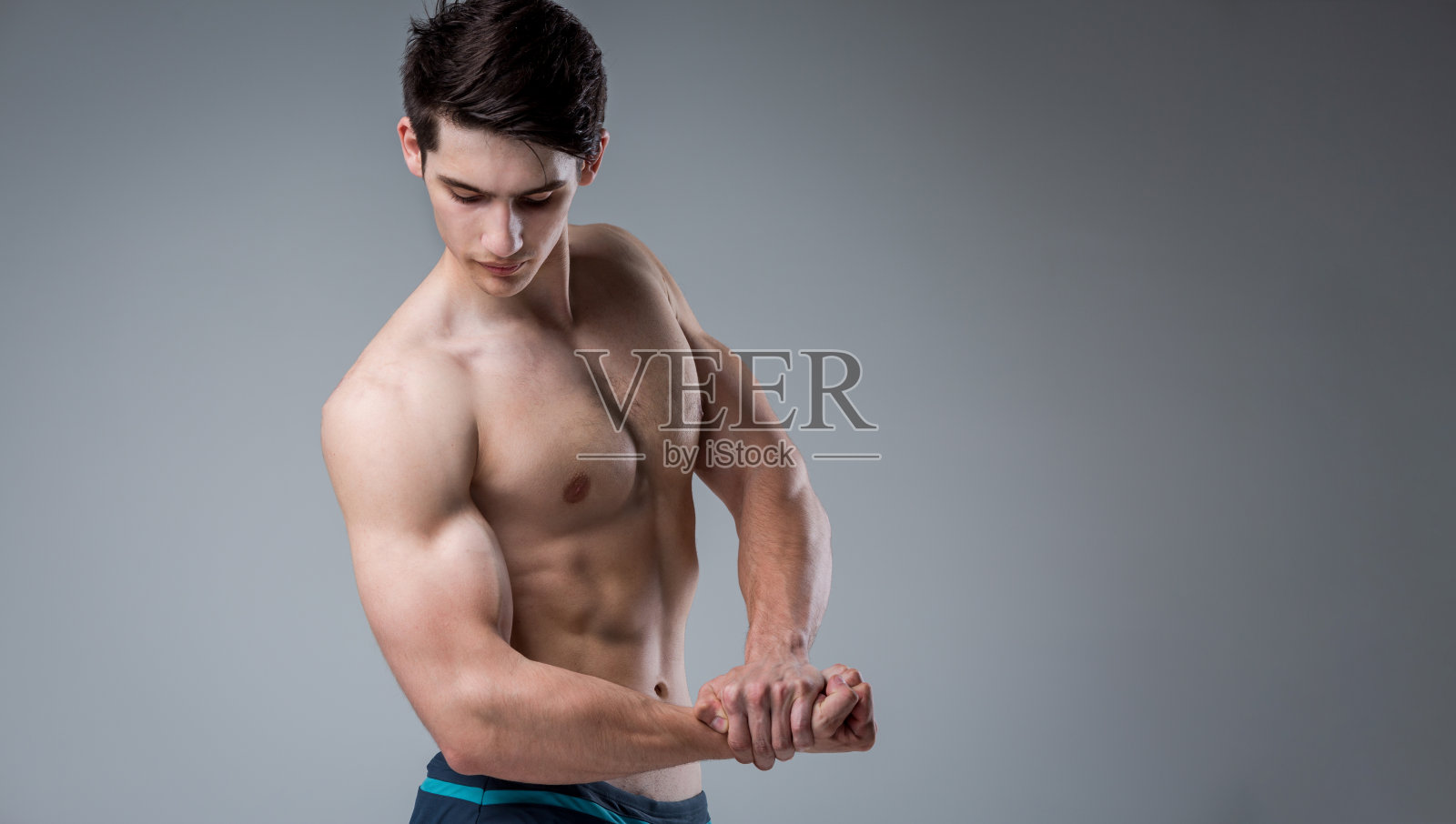 年轻的男运动员健美姿势。英俊的、健壮的、有力量的男人。健身肌肉发达的人。年轻运动员在演播室展示肌肉。六块肌肉在灰色背景下赤裸上身摆姿势照片摄影图片