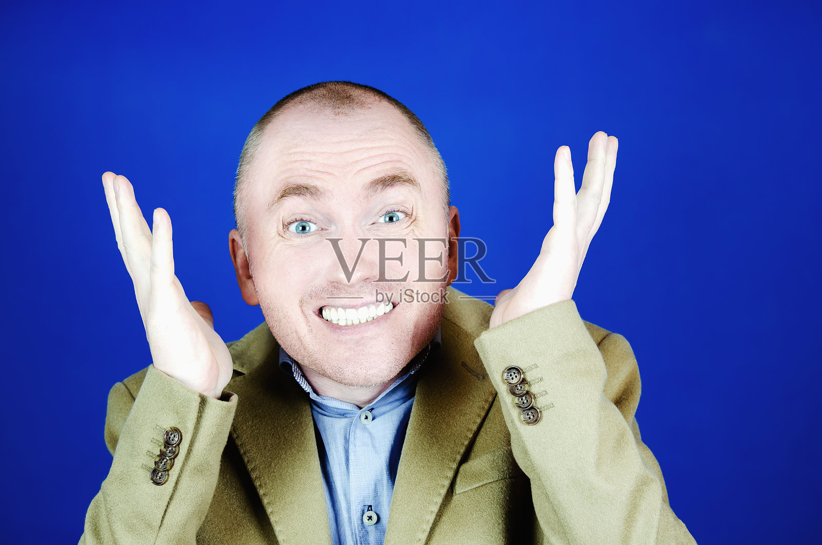 一个穿着奶油色外套的惊讶的男人在蓝色的背景上举起他的双手。为您的广告，口号或促销空白的地方照片摄影图片